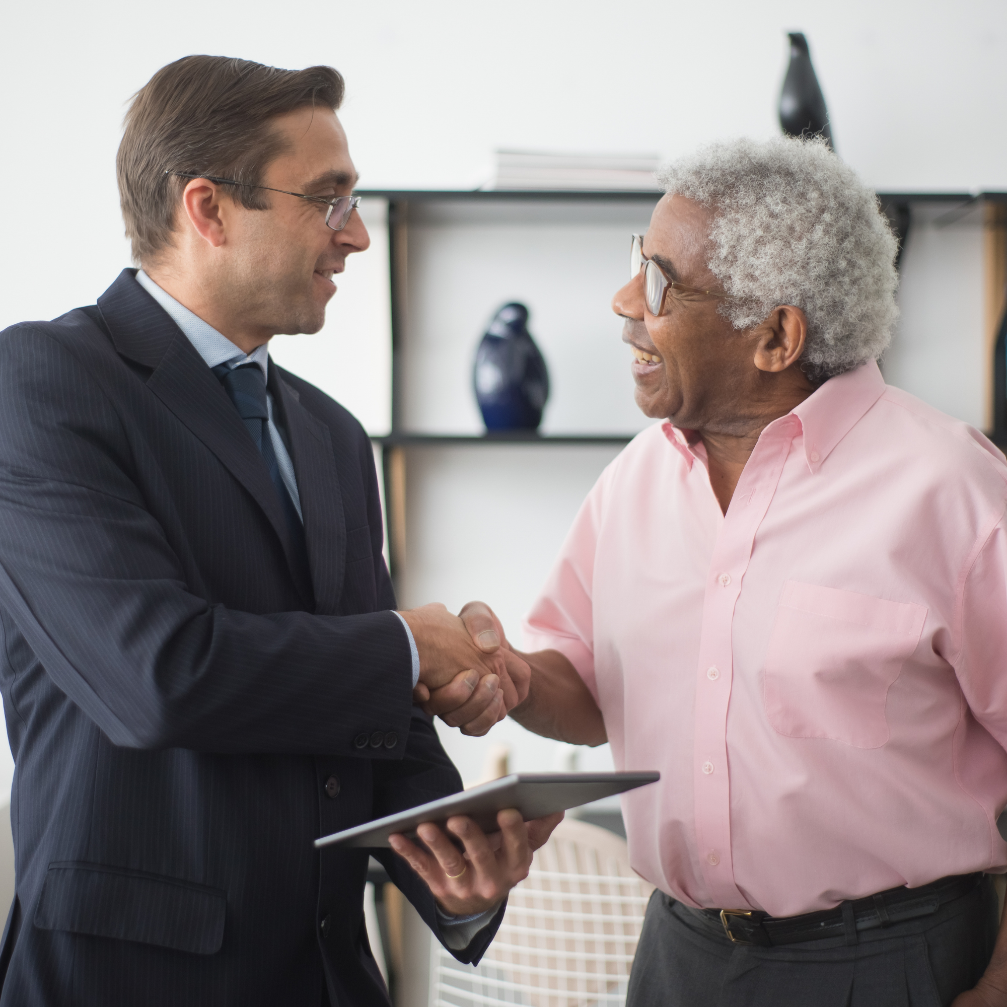 Two men in business attire shaking hands in an office setting.