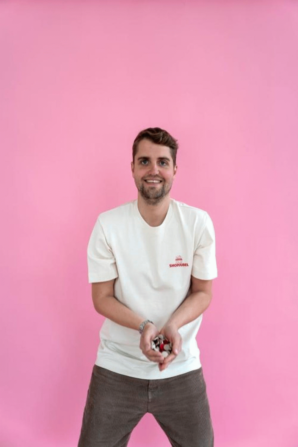Ein Mann steht vor einem pinken Hintergrund, trägt ein weißes T-Shirt und hält einen Schlüsselbund in den Händen. Er lächelt in die Kamera.