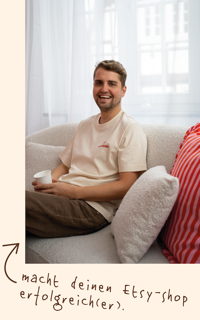 Ein lachender Mann sitzt auf einem Sofa, hält eine Tasse in der Hand, vor einem Fenster mit weißen Vorhängen.