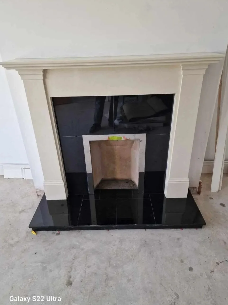 Fireplace with black tiles and a white mantel in a room under construction.