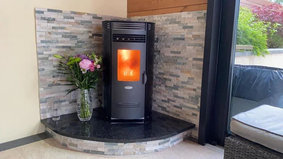 A modern corner fireplace with a black surround and a stone facade, next to a glass vase with pink and purple flowers, situated on a black marble hearth.