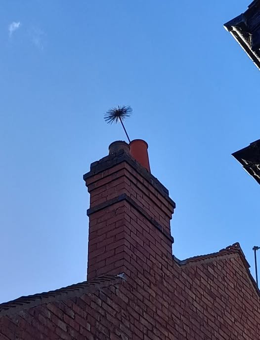 A brick chimney with a chimney sweep brush at the top, against a clear blue sky.