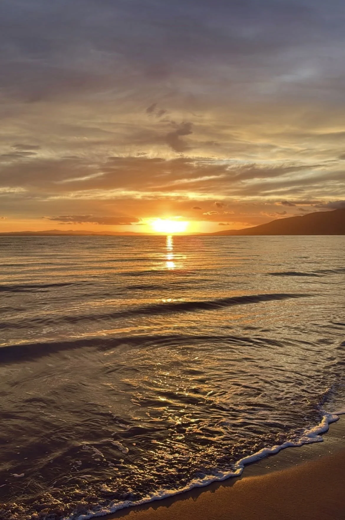 Sunset over the ocean with colorful sky, calm waves reaching the sandy beach.