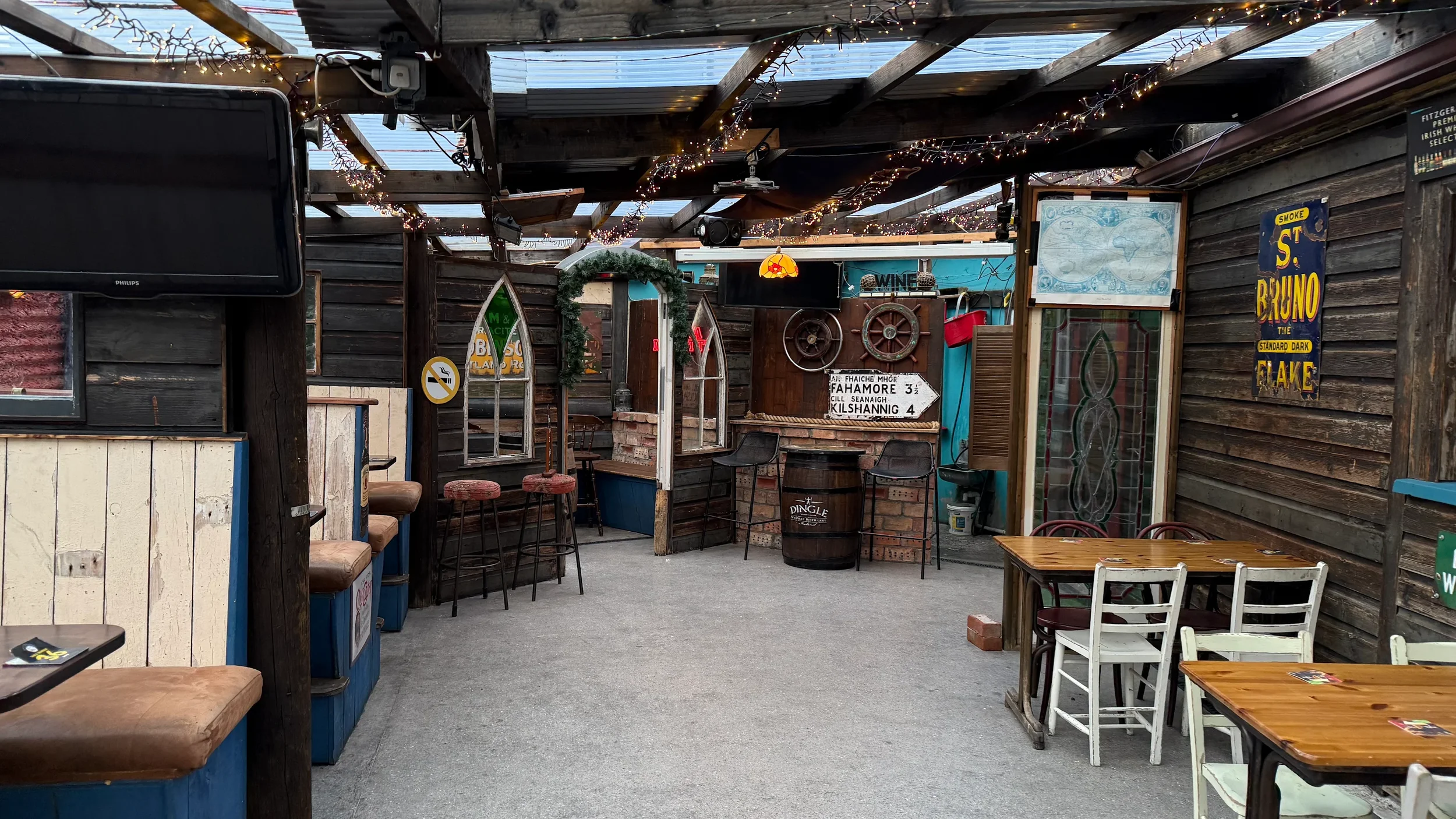 Decorated outdoor patio with wooden walls, string lights, tables, chairs, a TV, and vintage signage.