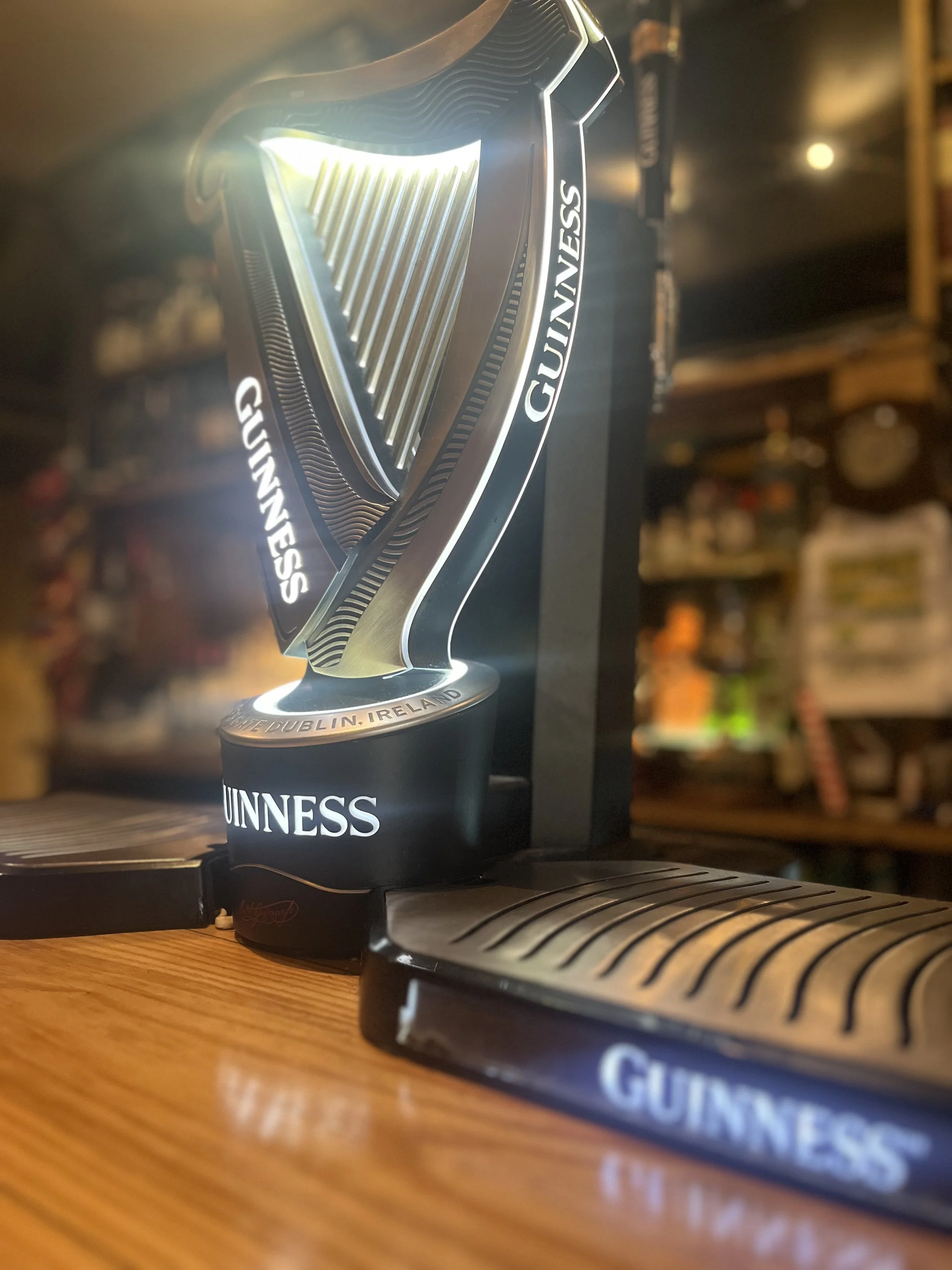 Guinness Irish stout advertising display with a large illuminated Guinness harp logo and branding on a wooden bar counter.