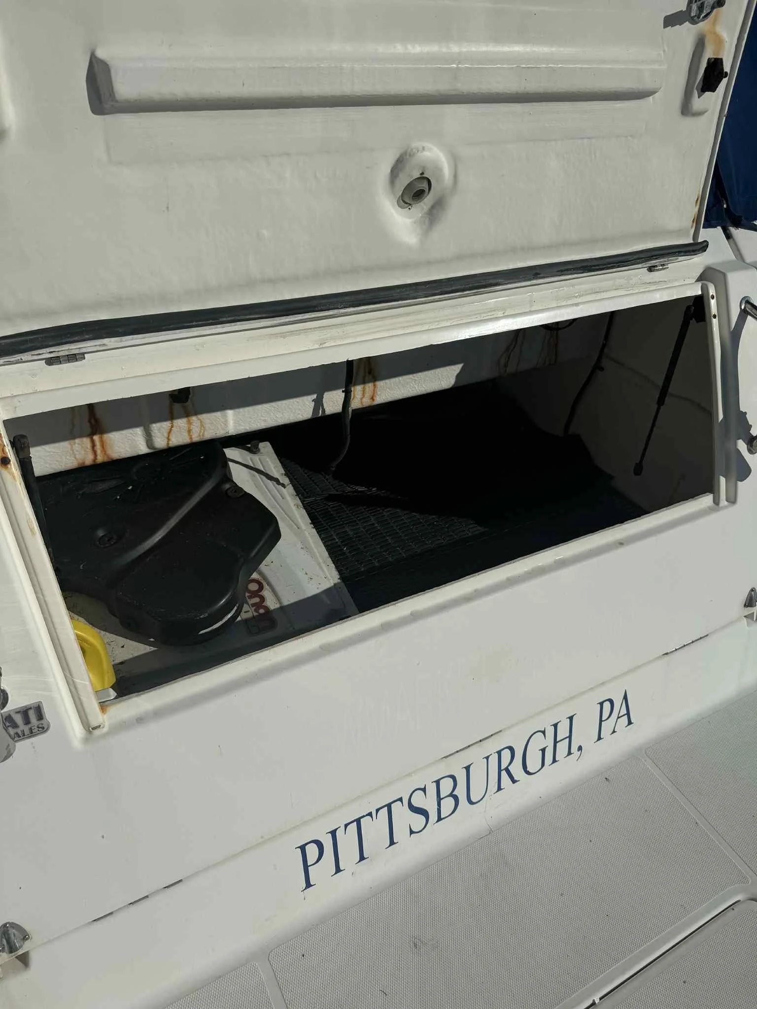 Open storage compartment on a boat with a black motor, a yellow item, and a net inside, with "PITTSBURGH, PA" written on the exterior.