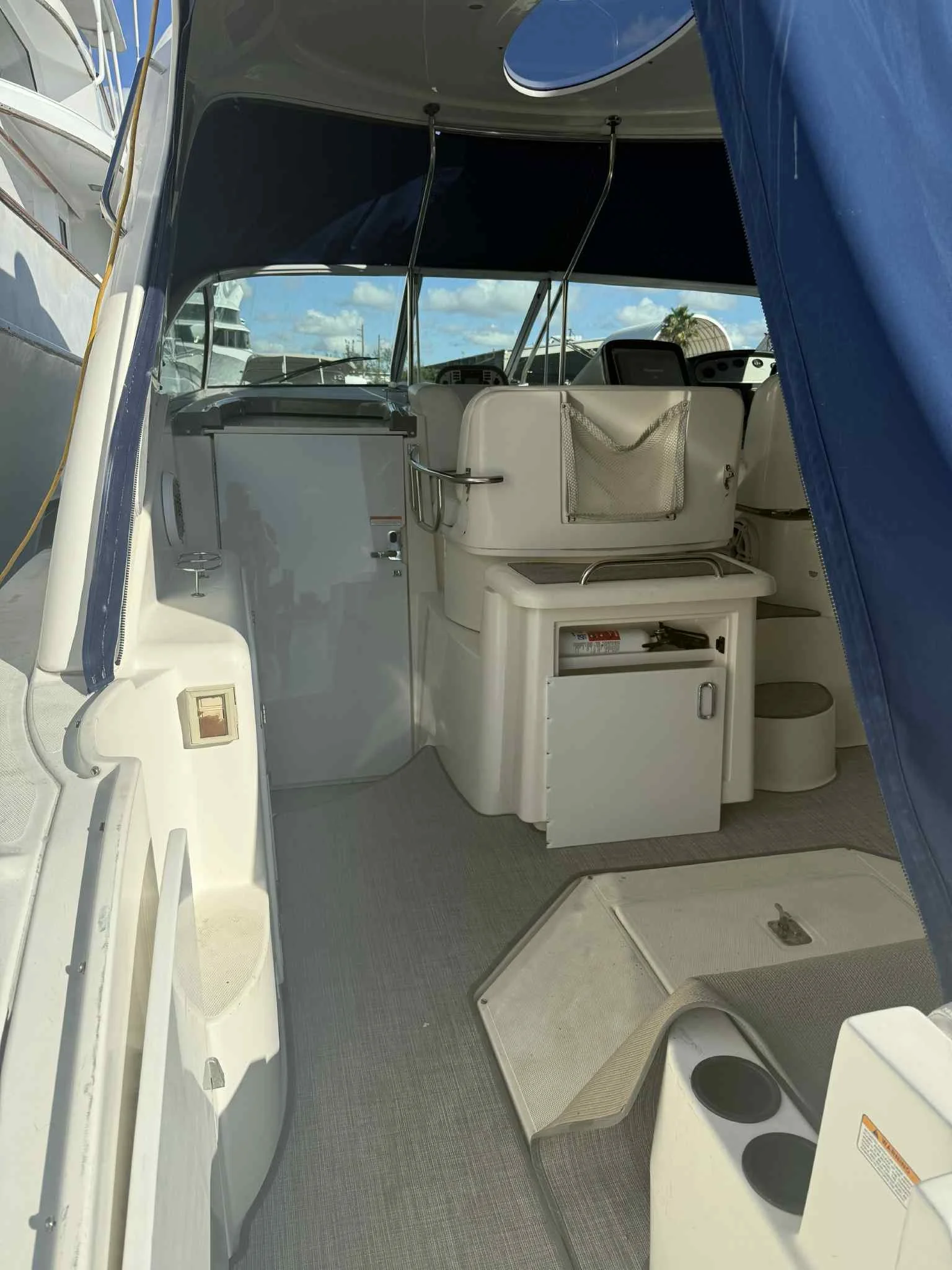 Interior of a boat with a small kitchenette, seating area, and navigation controls, covered partly by a blue canopy.