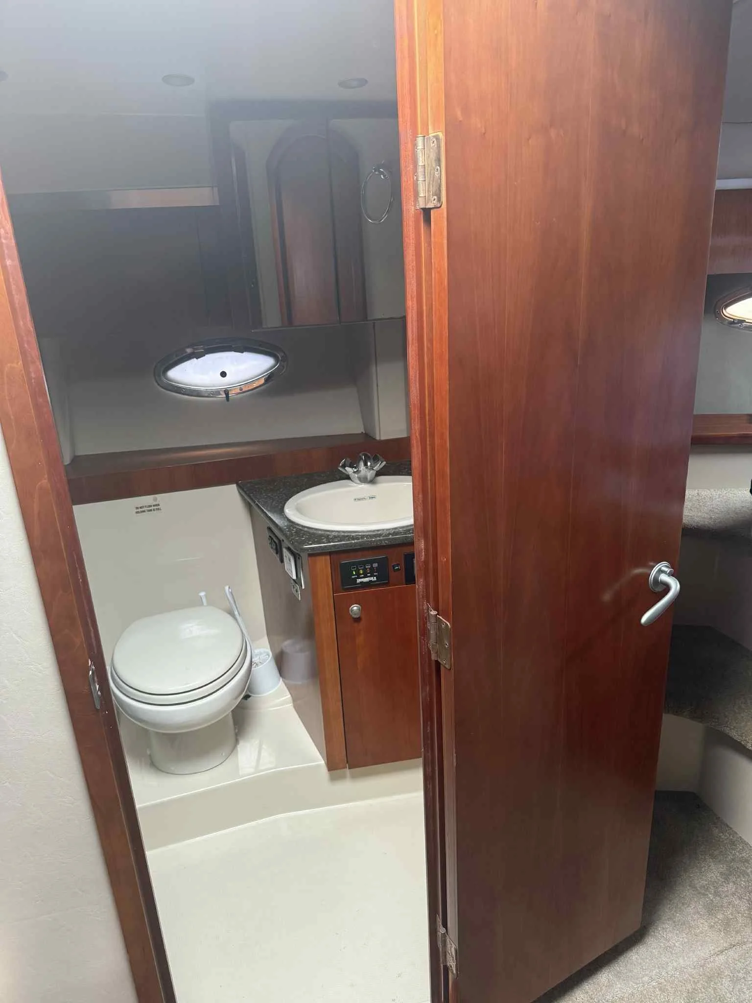 Small bathroom with a toilet, sink, mirror, and wooden door, inside an RV or boat.