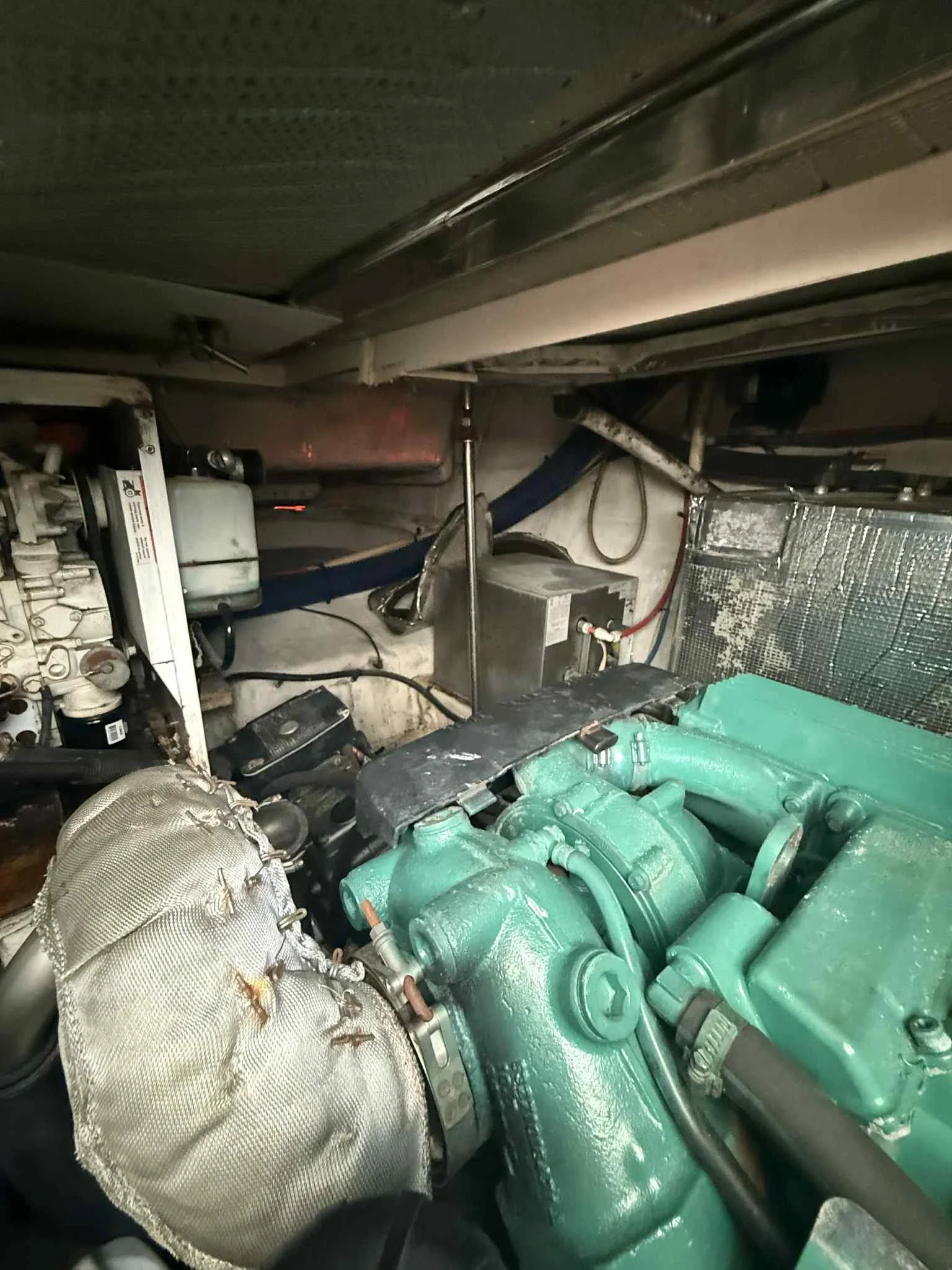 Engine room with a green engine, metal components, wiring, and a reflective heat shield.