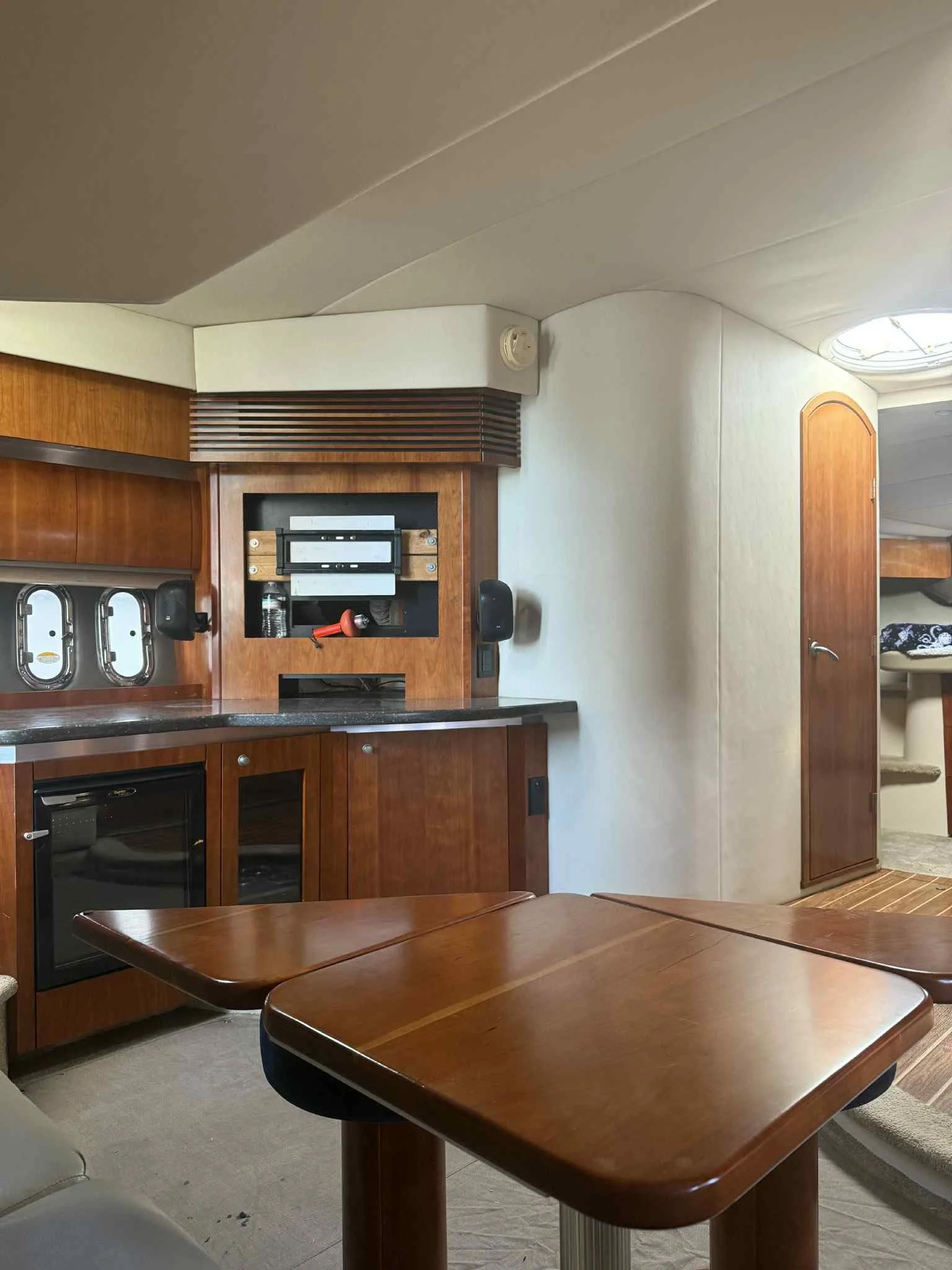 Interior of a boat or yacht cabin with wooden cabinetry, a small table, and a door leading to a sleeping area.