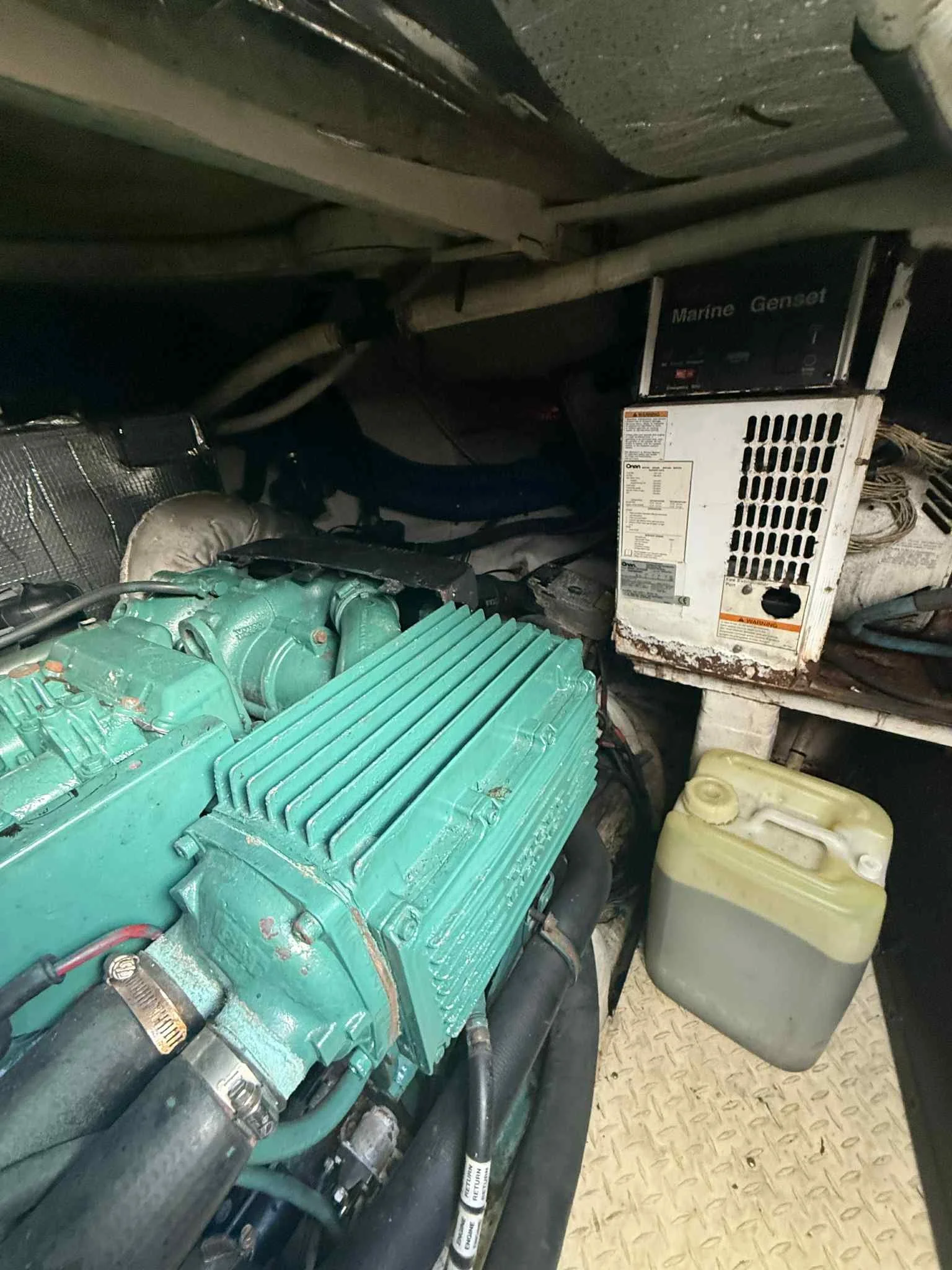 View of a boat engine compartment with a green engine, a white generator labeled 'Marine Genset,' and a yellow coolant reservoir.