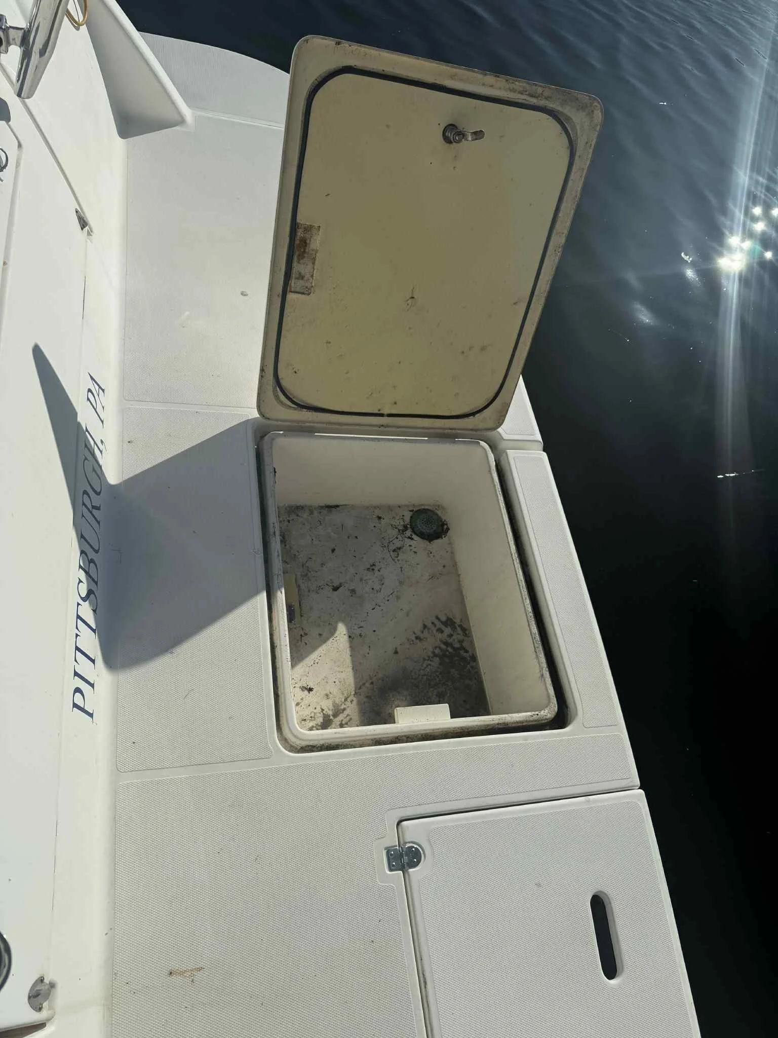 Open cooler on a boat with dirt and grime inside, with water and sunlight reflecting off the water in the background.