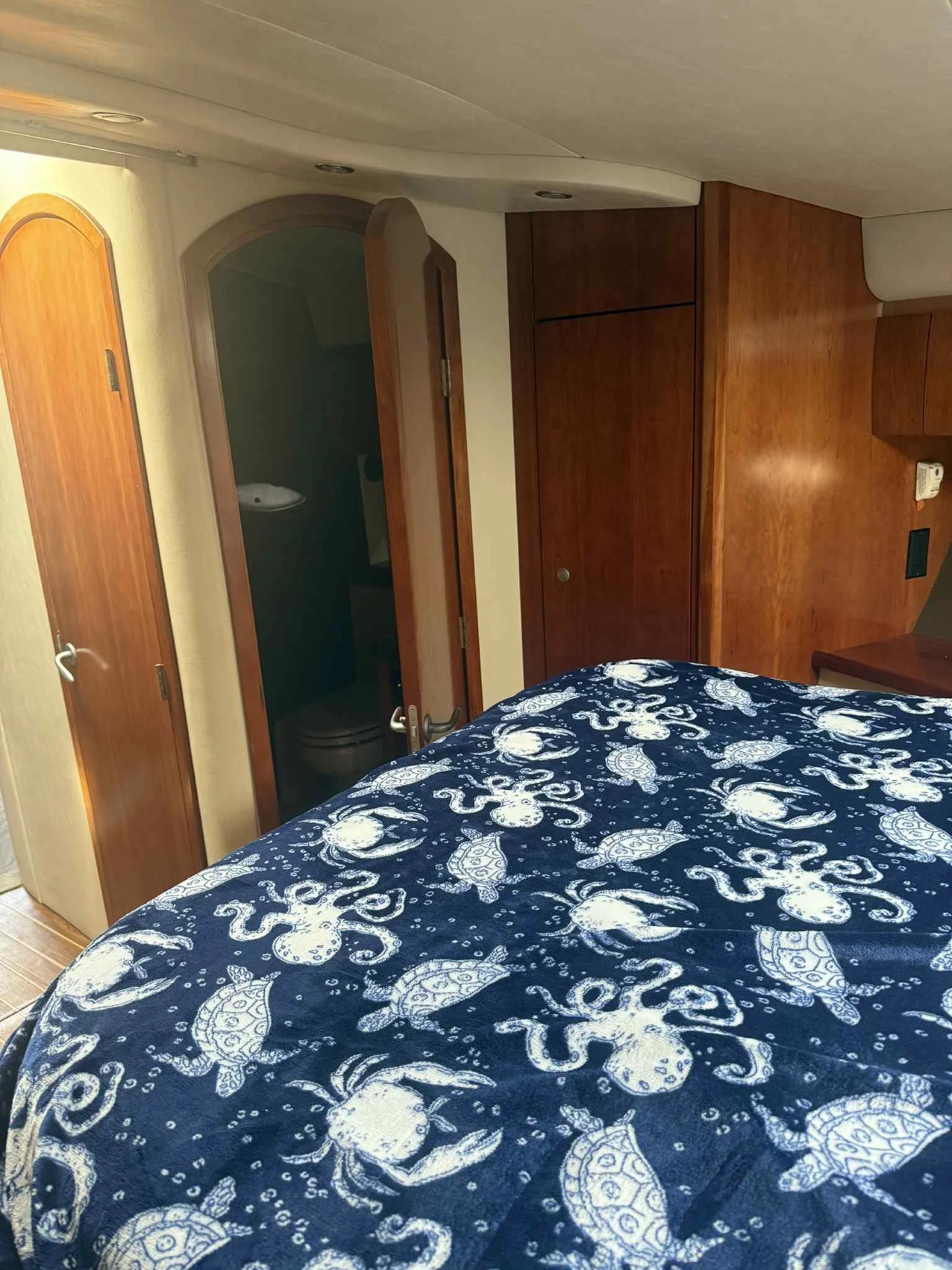 Bedroom with a bed covered in a navy blue and white sea turtle patterned blanket, wooden closet doors, a doorway to a bathroom, and wood-paneled walls.