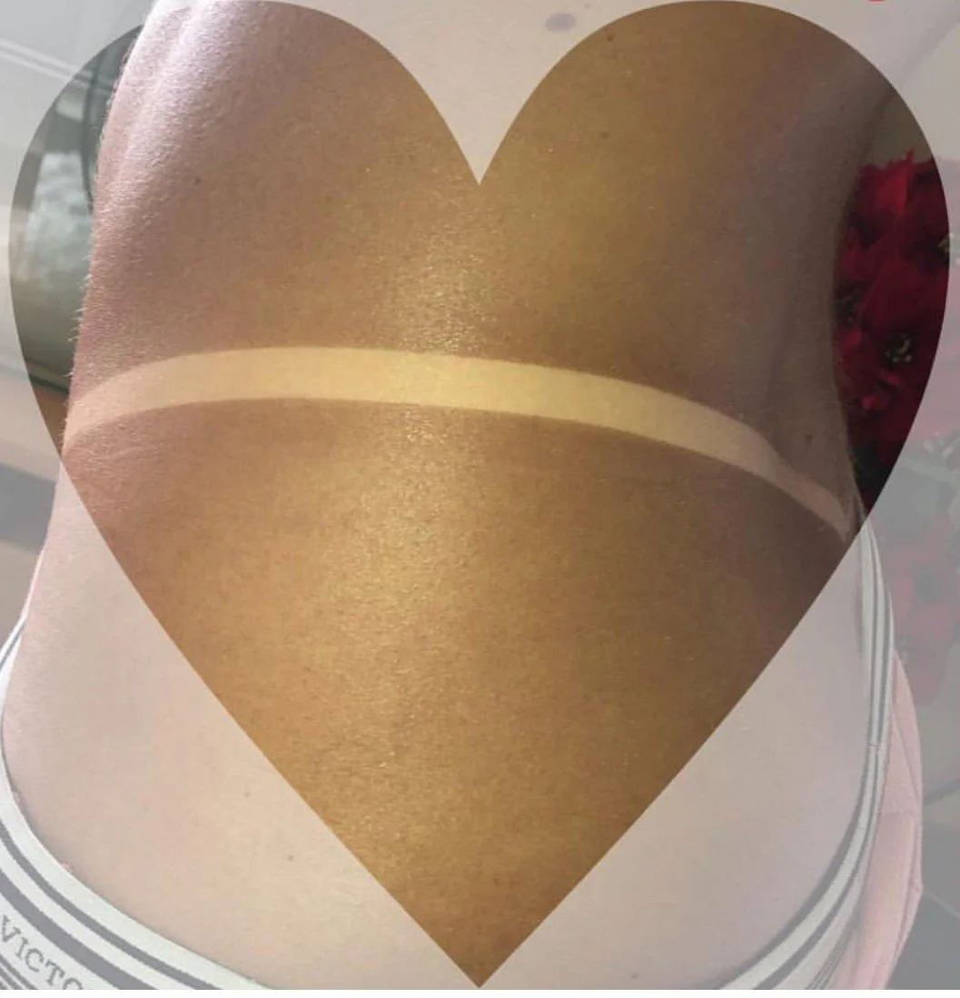 Close-up of a gold-colored thigh-high stocking with a beige band at the top, viewed through a heart-shaped cutout after a group mobile spray tanning session for her wedding.