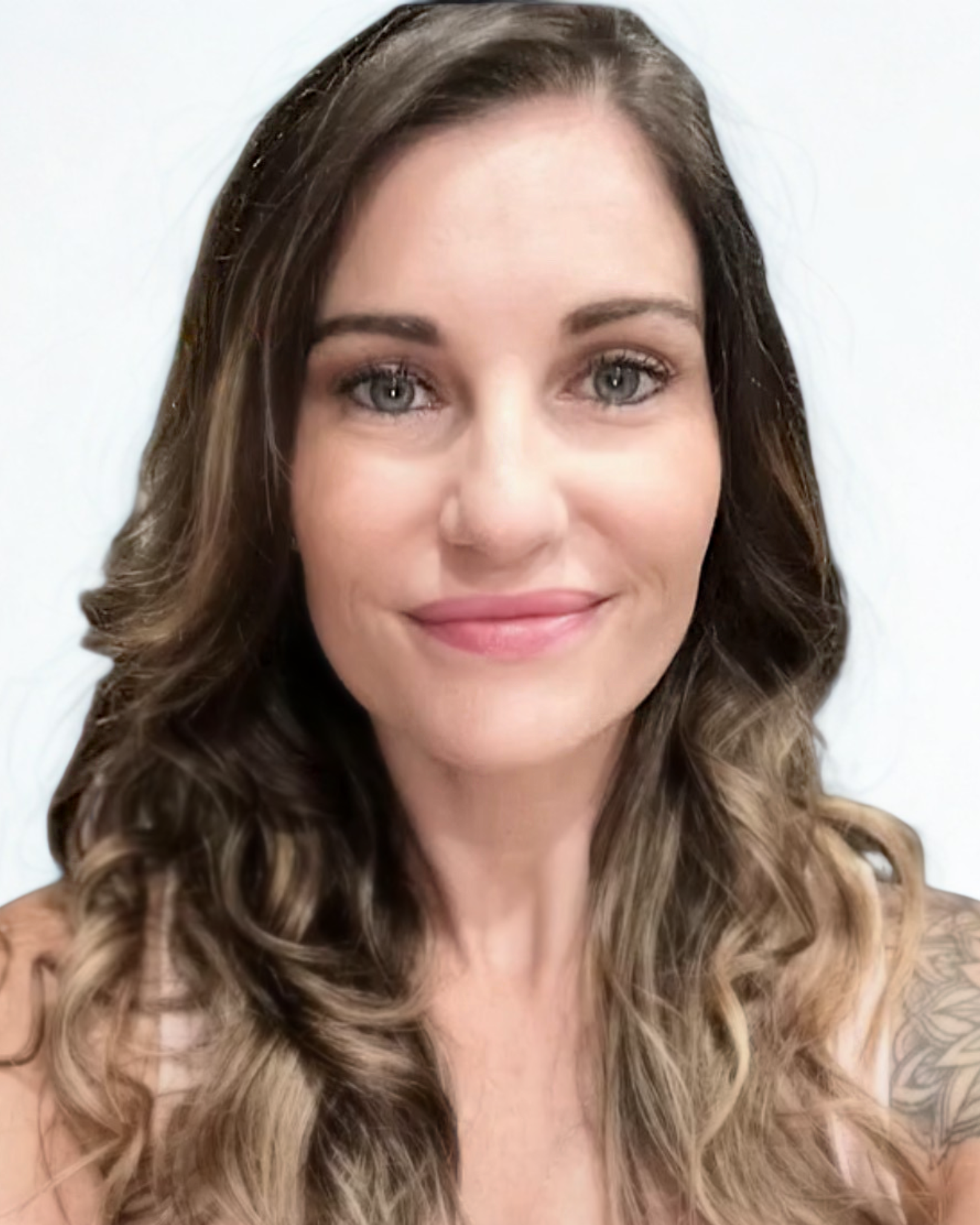 Close-up portrait of a woman with long, wavy brown hair and light blue eyes, smiling softly against a plain white background.