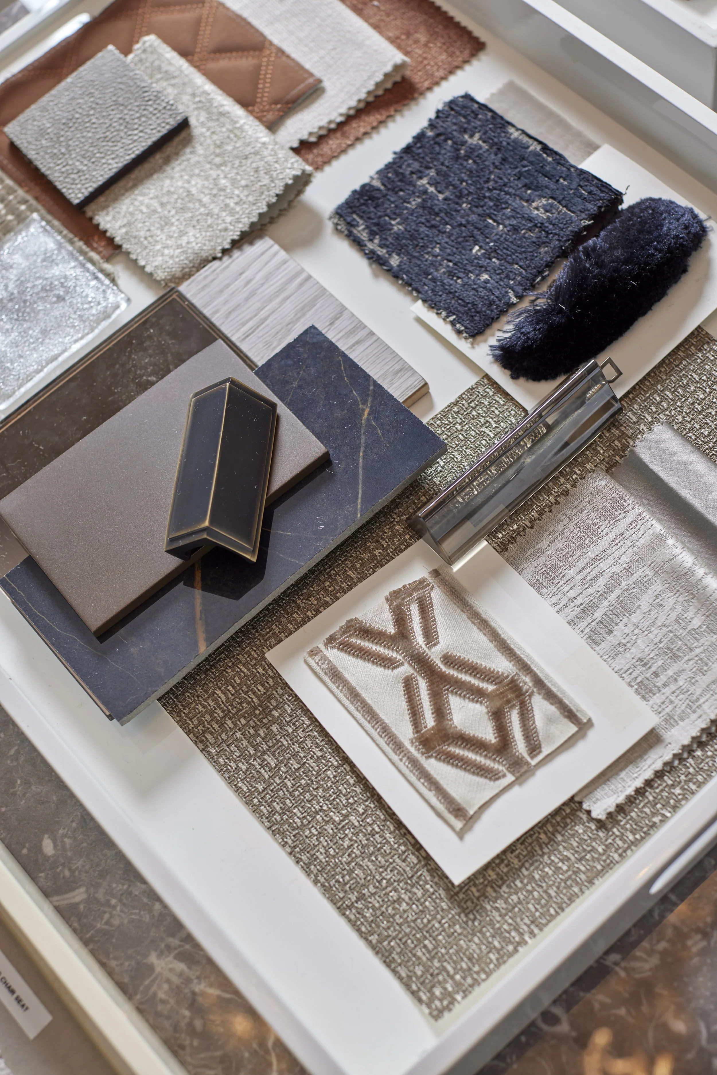 A selection of interior design samples, including fabric swatches, tile and stone samples, and decorative materials arranged on a white tray.