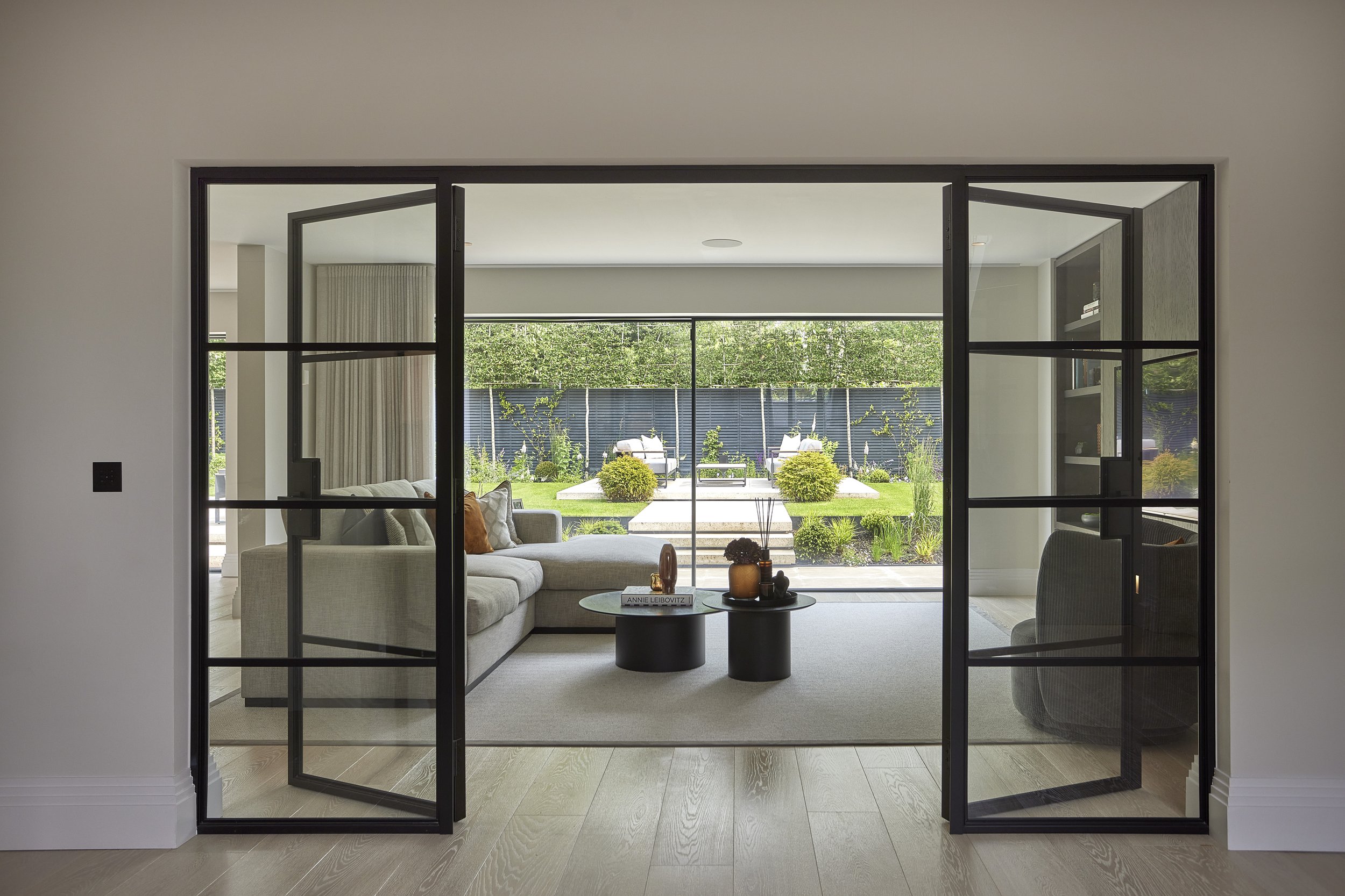 Living room with glass double doors opening to a backyard with plants, steps, and outdoor seating.