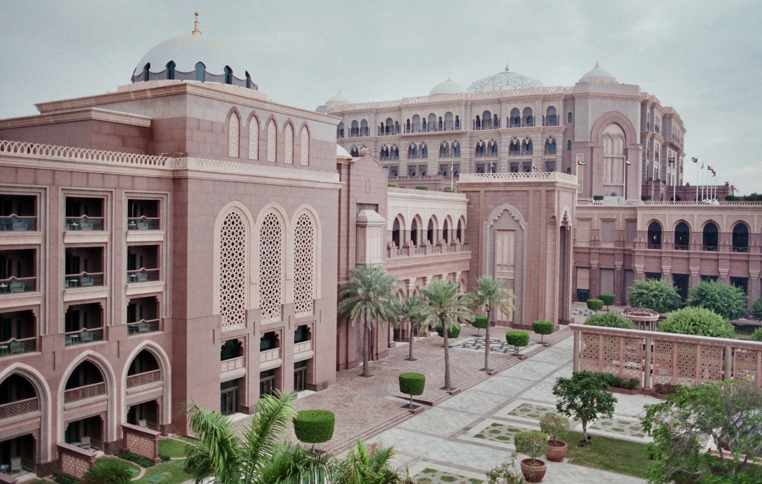 Pink Middle Eastern style hotel or building with palm trees and landscaped courtyard.