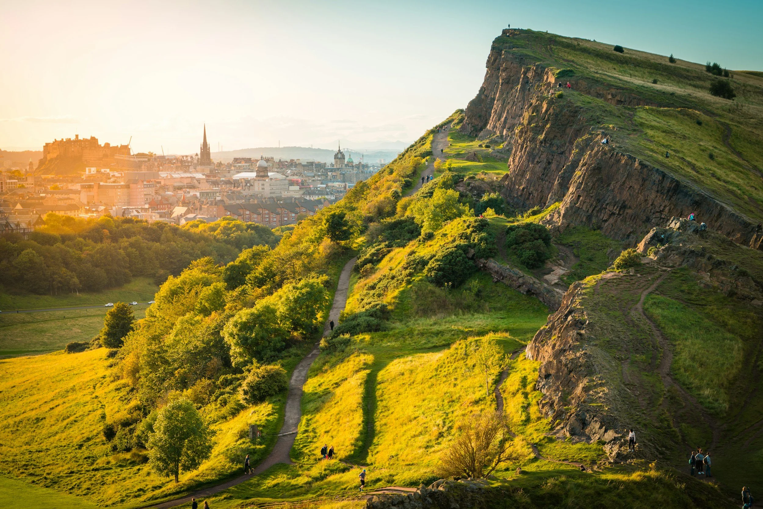 A scenic view of Arthur's Seat hill with a cityscape in the background at sunset