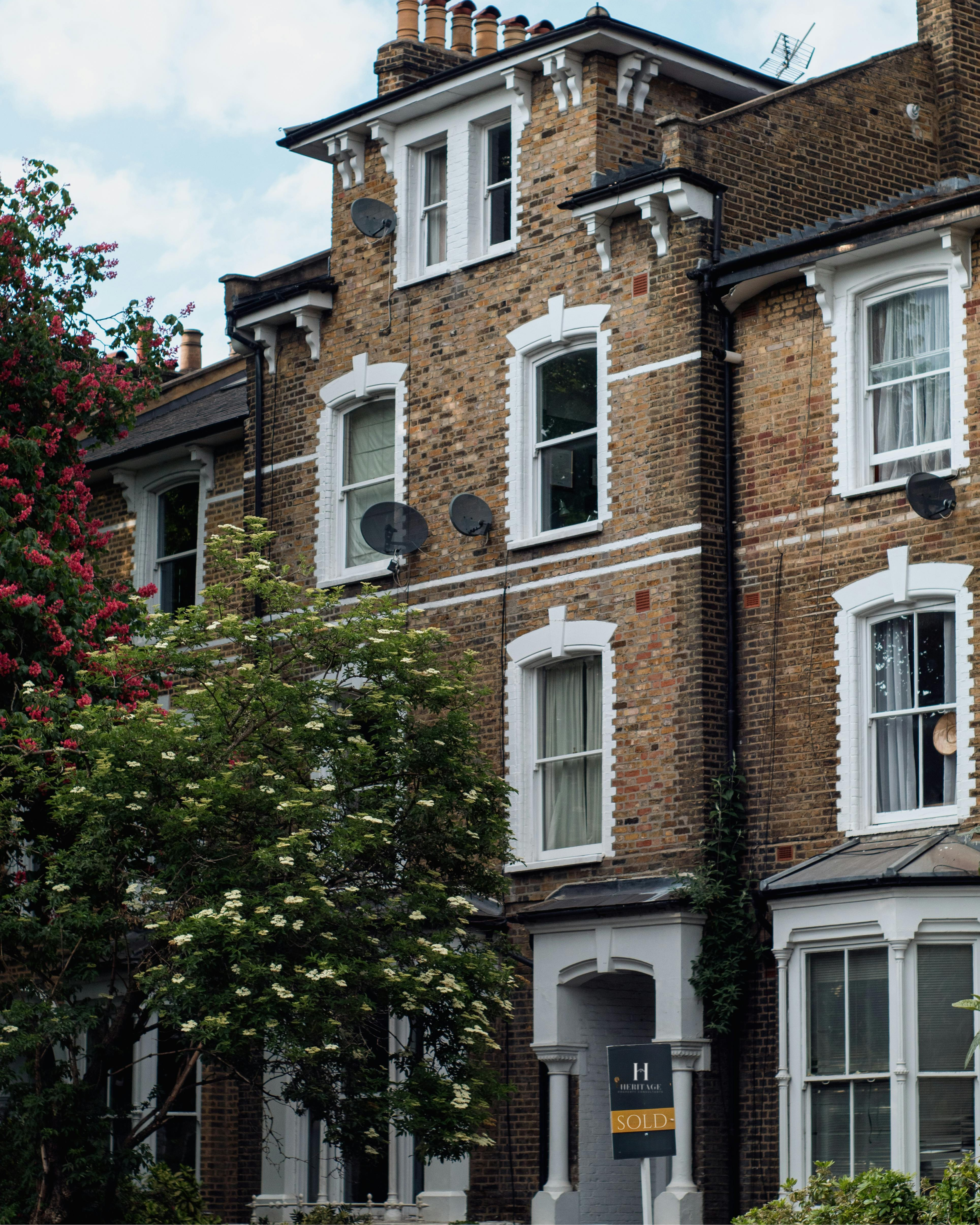 A brick residential building with white window frames and decorative trim, multiple satellite dishes on the exterior wall, trees in front, and a