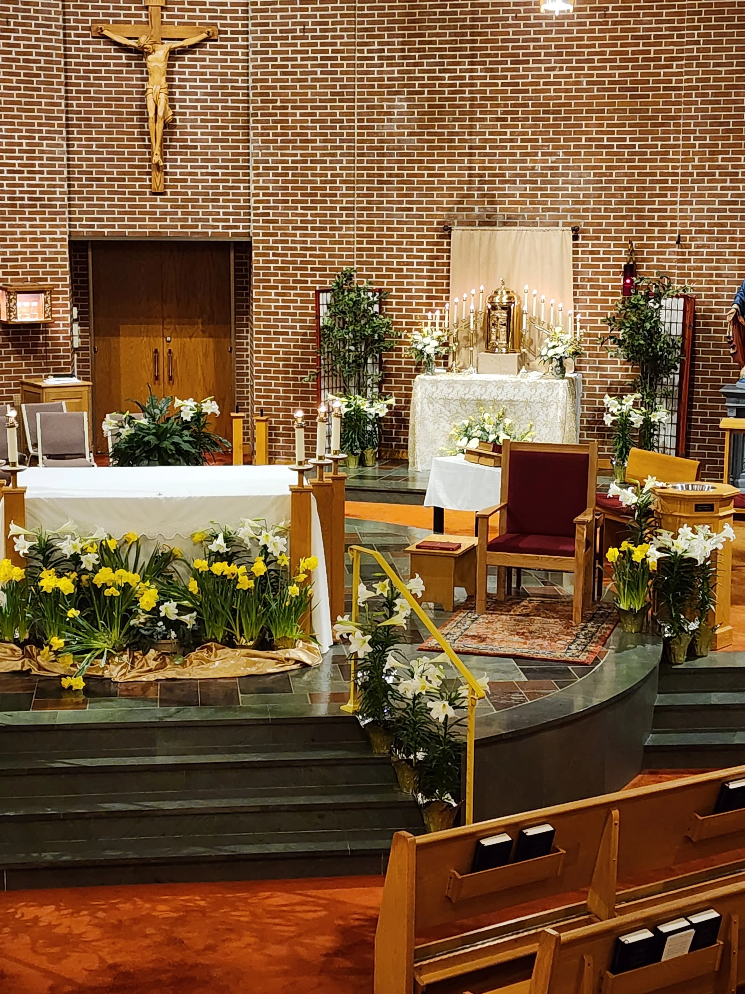Interior of a church altar decorated for a religious ceremony with flowers, candles, and a crucifix on a brick wall background.