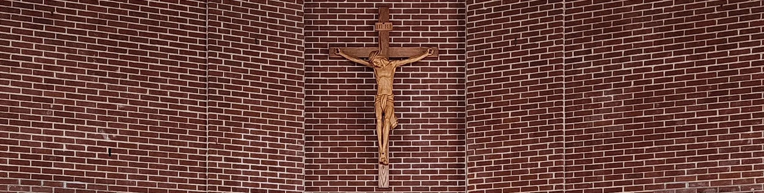 Wooden crucifix with Jesus figure mounted on a red brick wall inside a church.