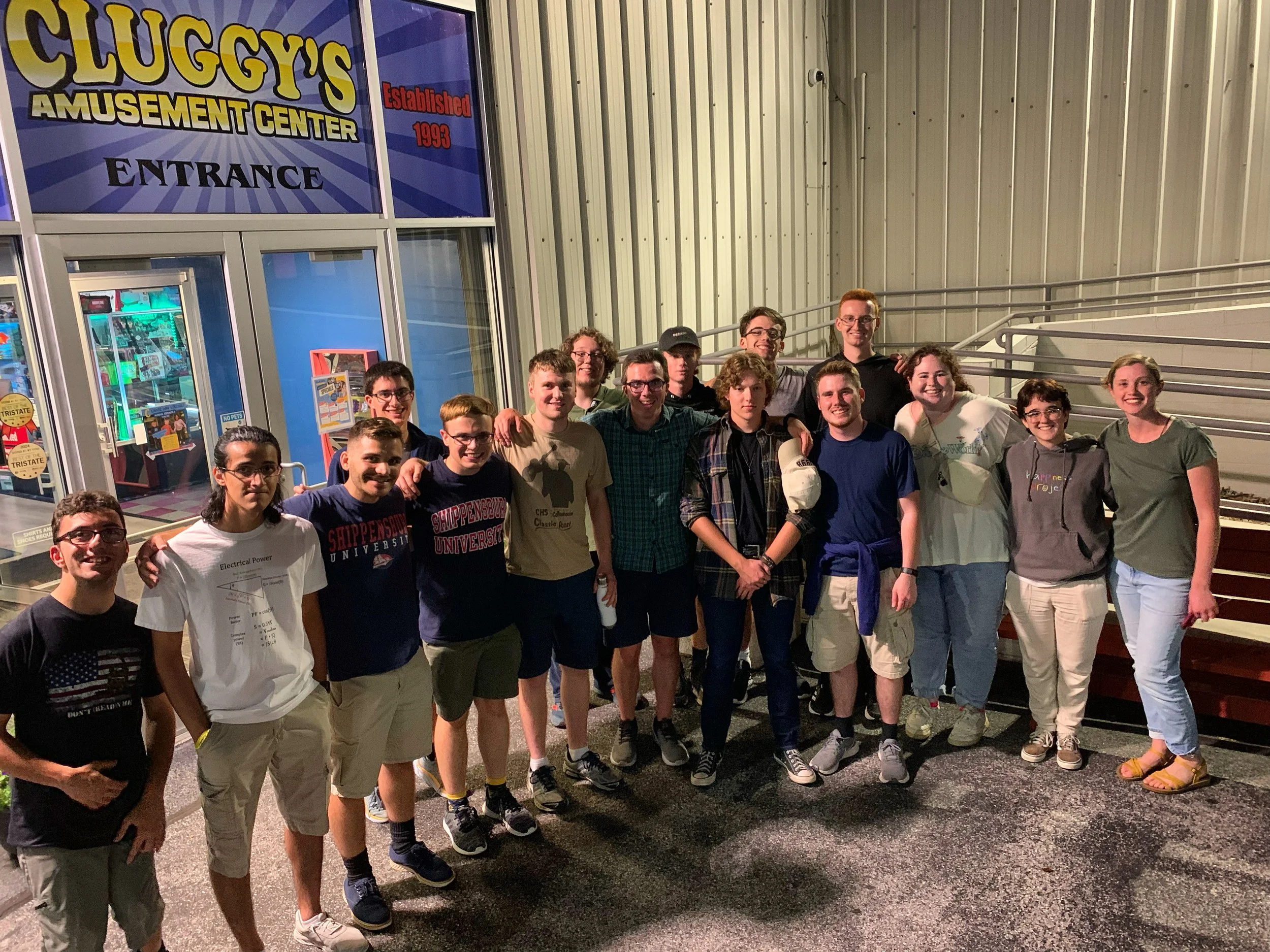 A group of young adults standing outside Cluggy's Amusement Center at night, posing for a photo.