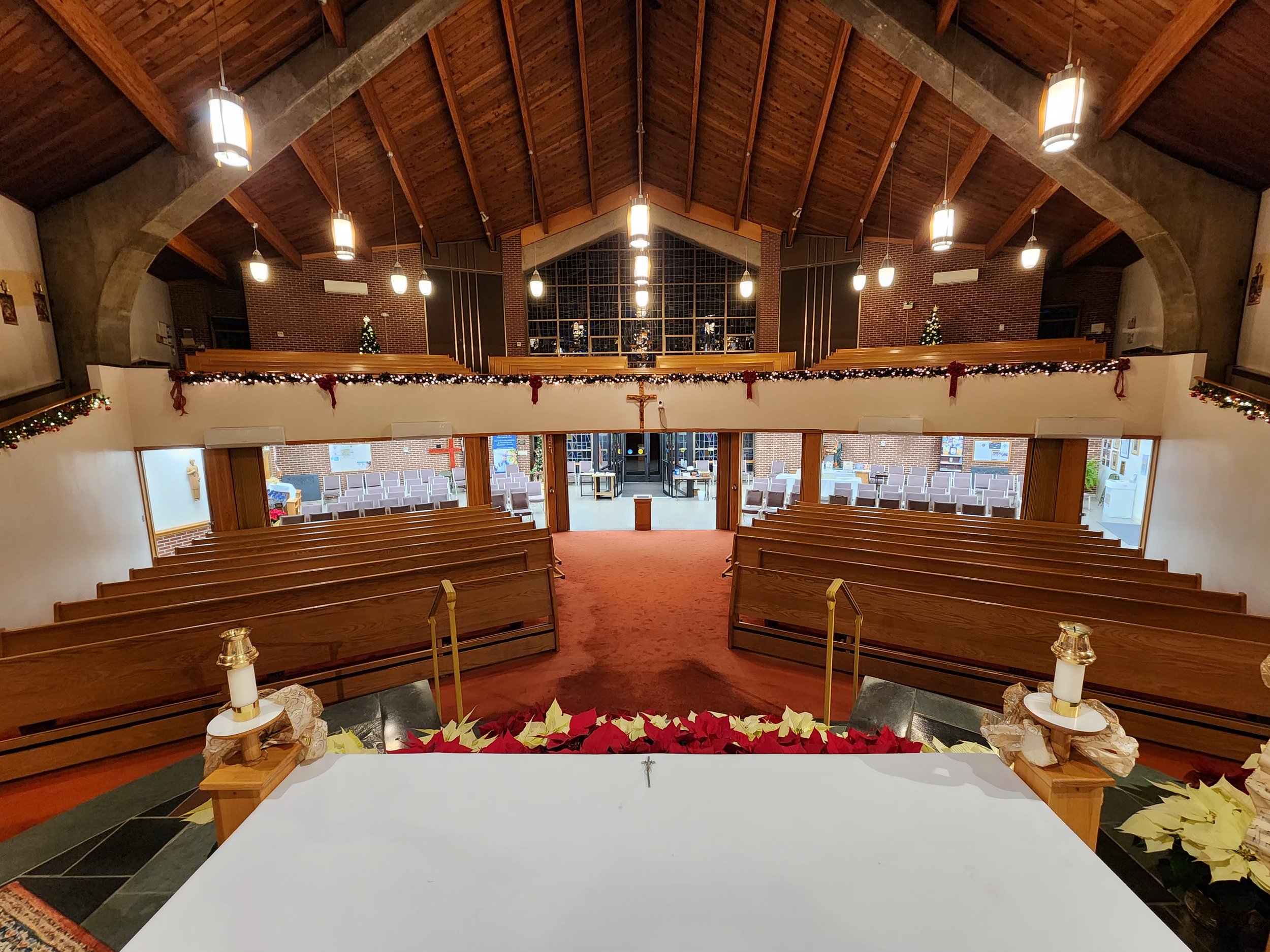 Interior of a church decorated for Christmas with poinsettias, garlands, and lights, view from the altar facing the pews and choir area.