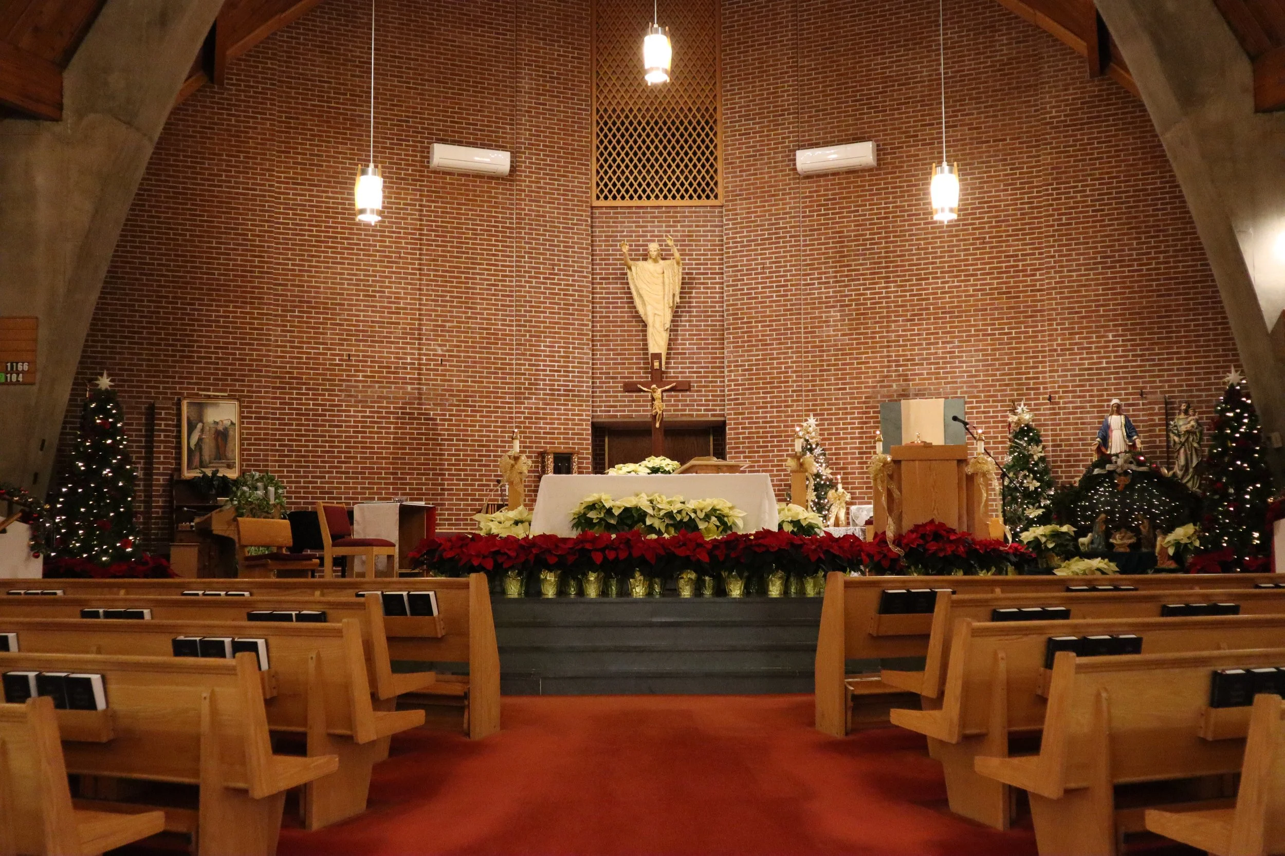 Interior of a church decorated for Christmas with an altar at the center, poinsettias, Christmas trees, statues, and religious symbols.