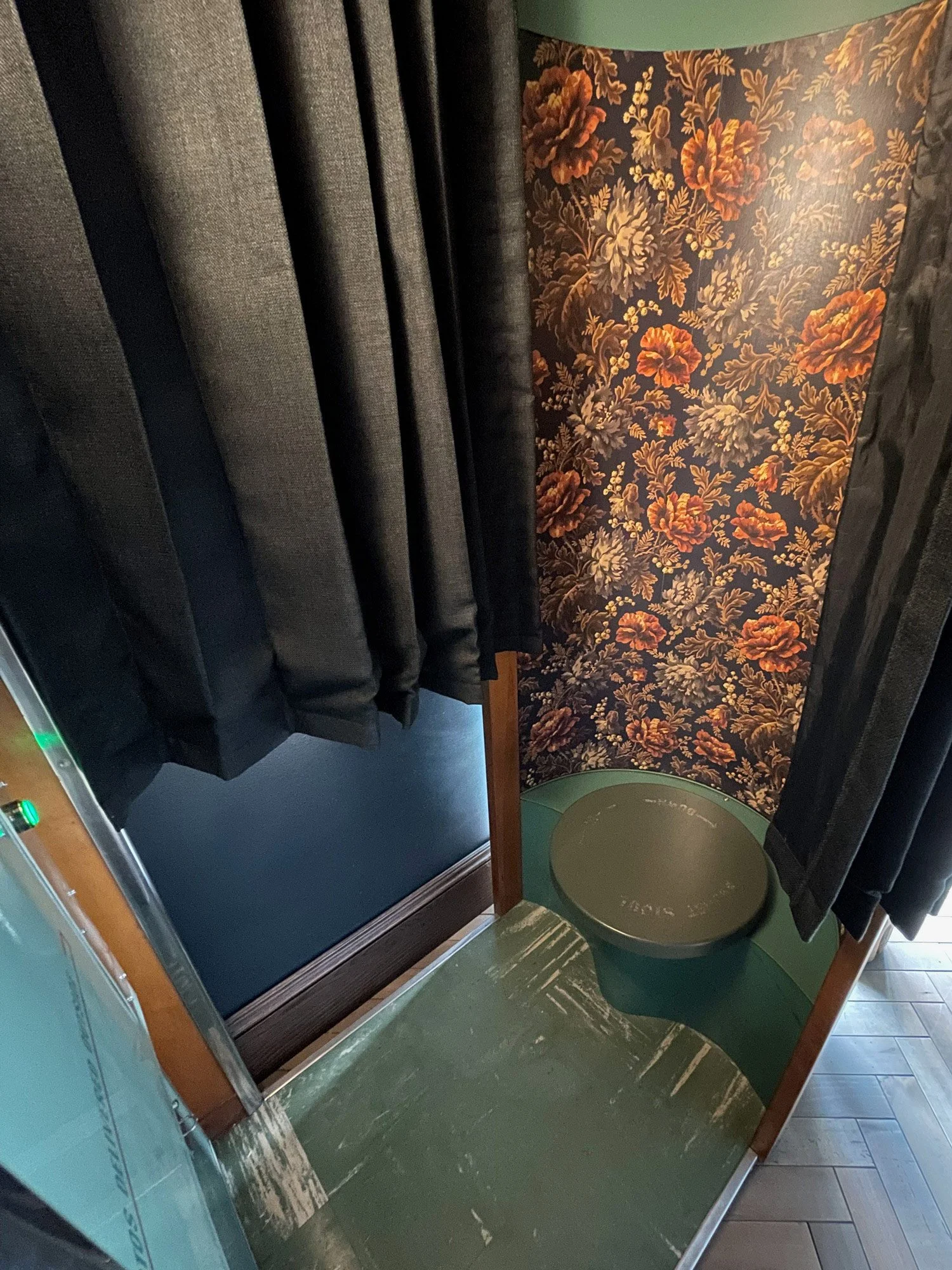 Auto-Photo Model 11 vintage photobooth interior with black curtains, floral wallpaper, and a round green footstool.