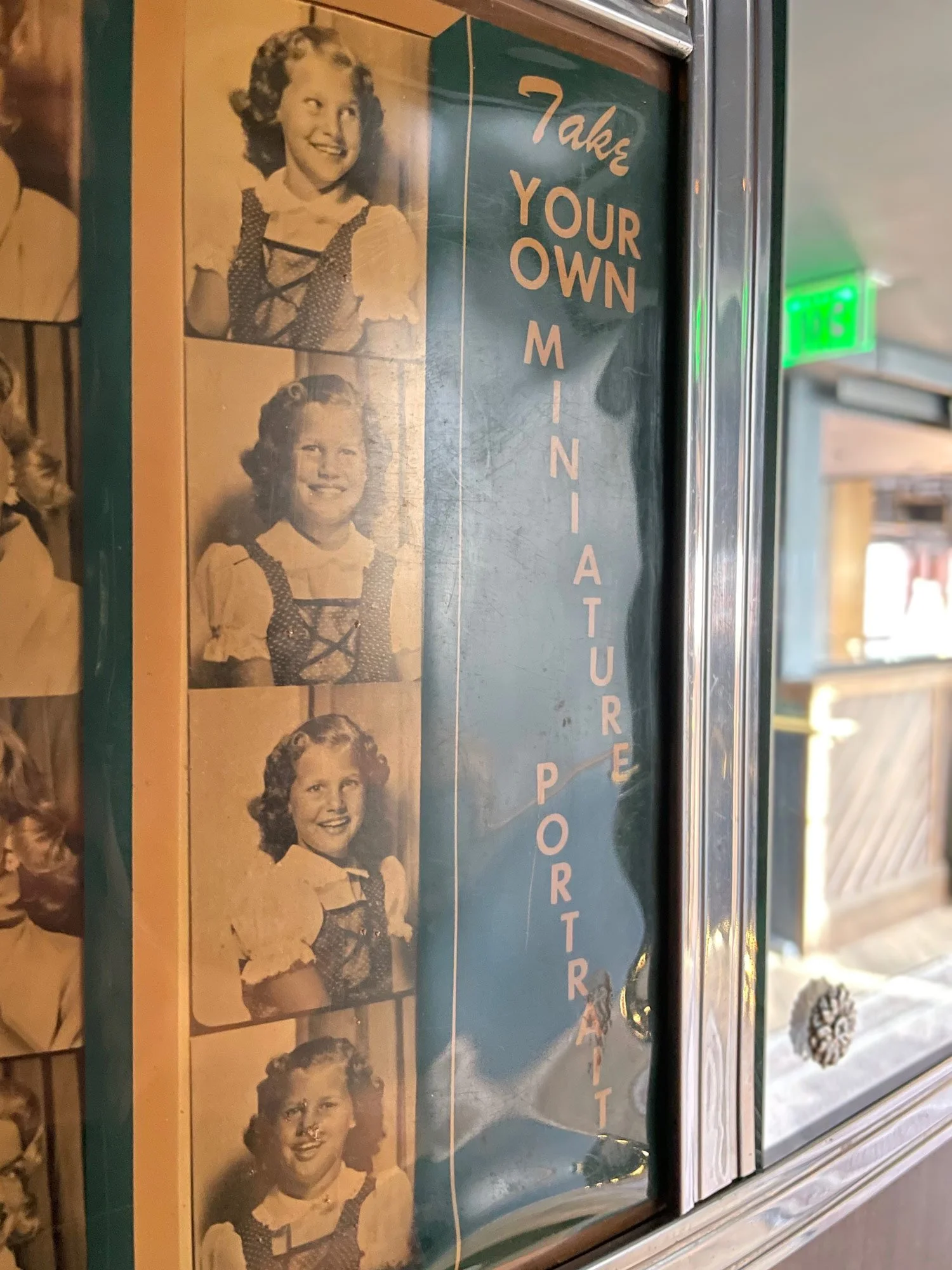 Auto-Photo Model 11 vintage photobooth signage featuring a strip of four black and white photos of a girl in different poses, along with the phrase 'Take Your Own Memory Portrait' beside them.
