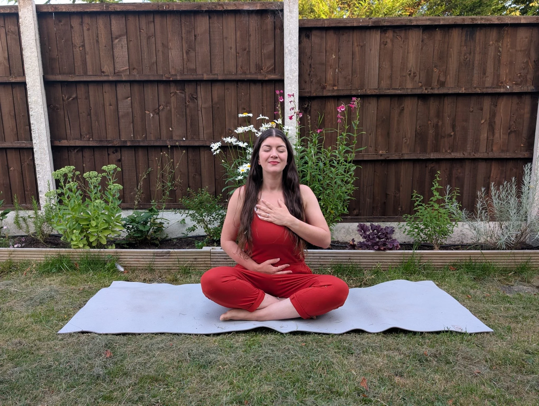 A woman in a garden sitting in a yoga pose on a yoga mat