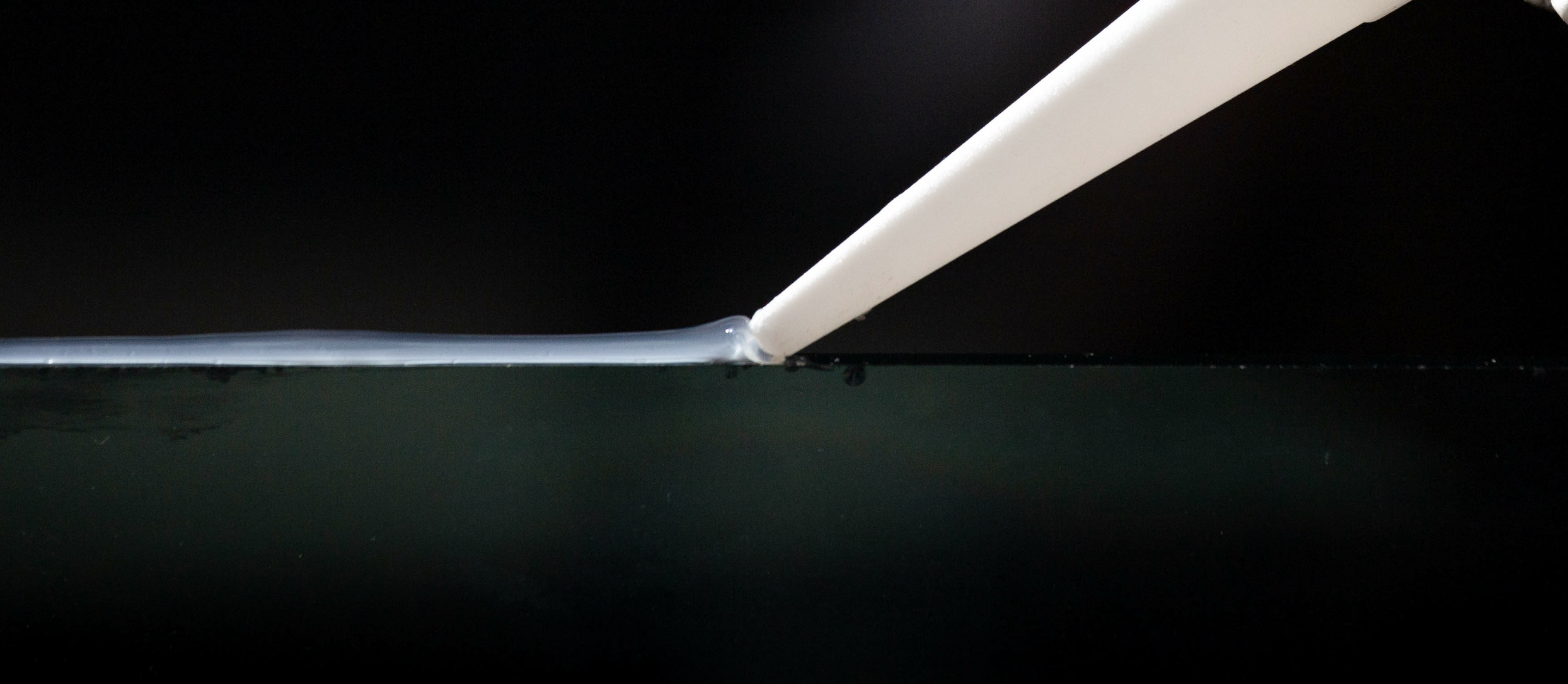 Close-up of caulk being applied to a glass surface with a caulk gun.