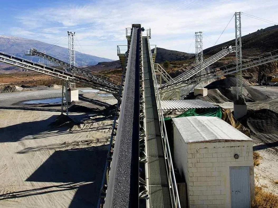 A large industrial conveyor system with multiple belts in an arid landscape, possibly for mining or processing materials.
