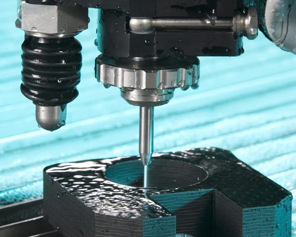 Close-up of a CNC machine milling a circular hole into a black metal block.