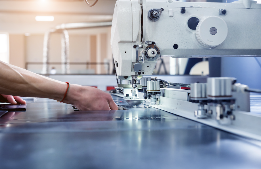 Close-up of industrial sewing machine stitching fabric in a factory setting.