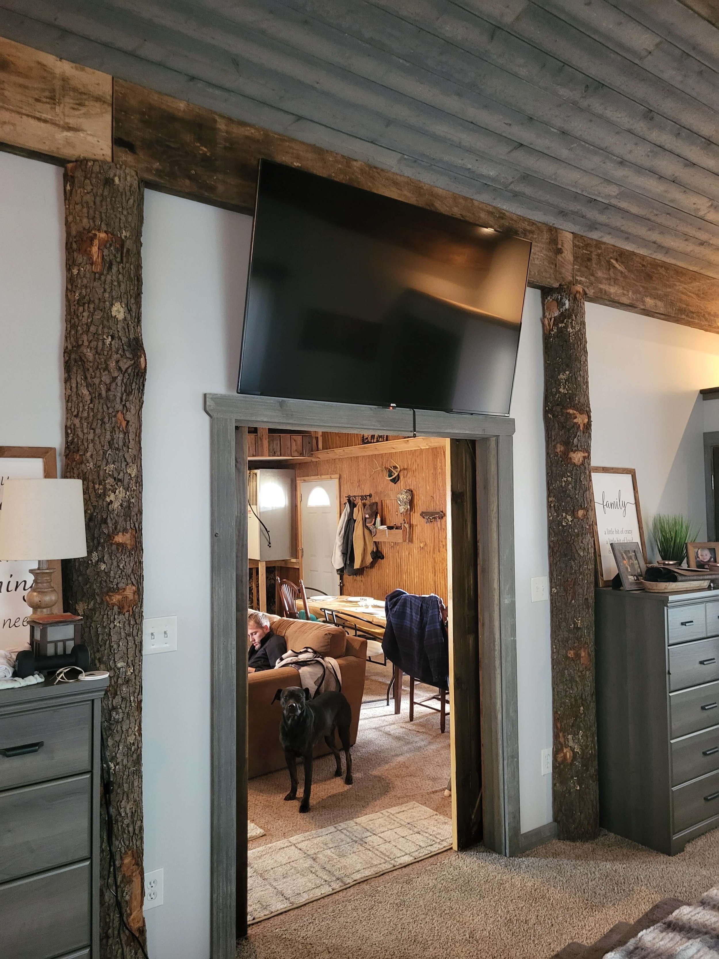 Interior of a custom master suite addition in Medina, Ohio highlighting rustic wood plank ceilings, natural log support pillars, and an open doorway leading to a living space by DLR.