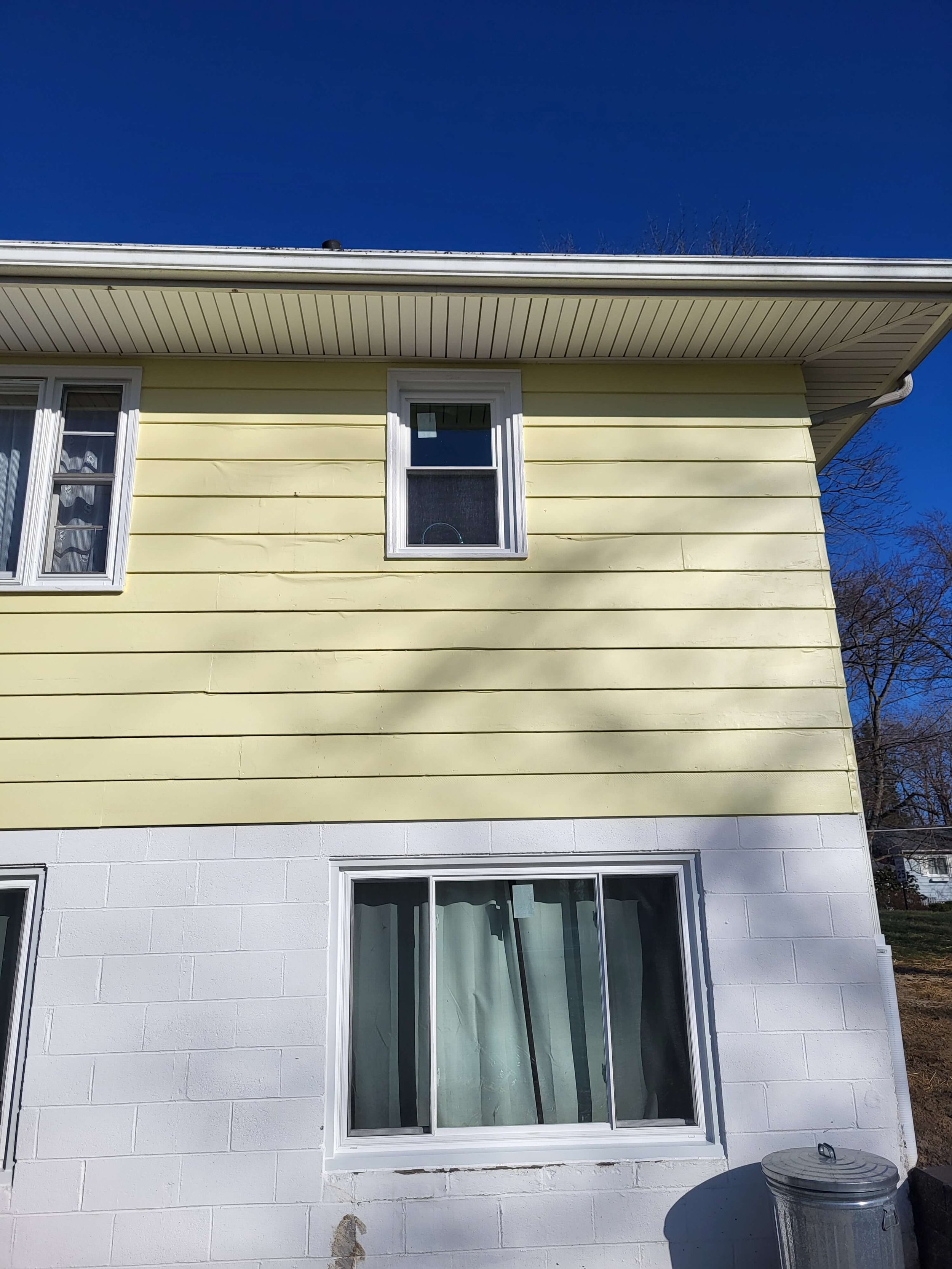 Full exterior side view of residential window replacement project on a yellow house with white foundation blocks in Cuyahoga Falls Ohio