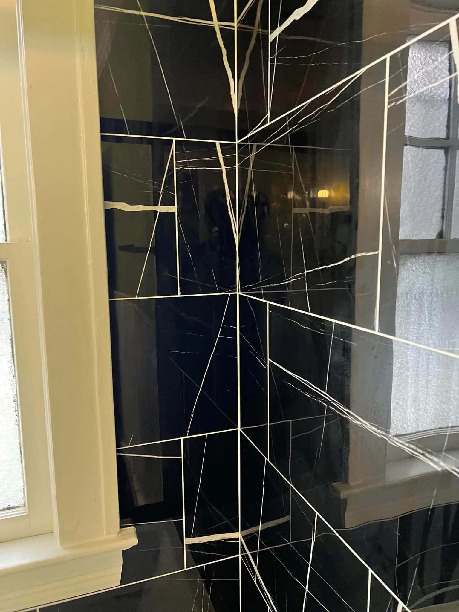 Close-up detail of black tiled shower walls with modern angled tile design and natural light from nearby window.