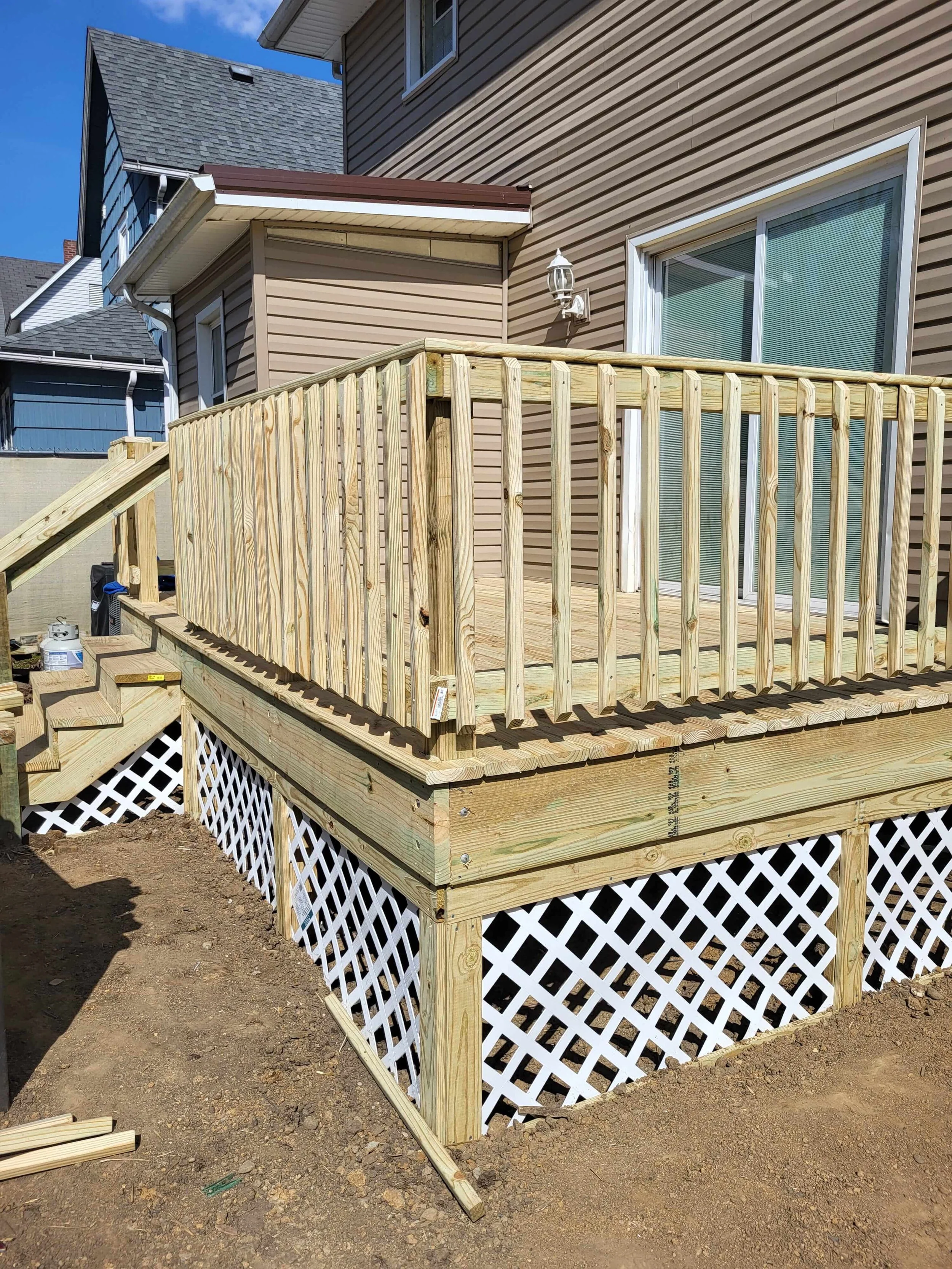 Ground-level view of the completed deck in Canton, Ohio showing the full installation including treated lumber boards, stairs, handrails, and the transition to the house wall with clean yard integration