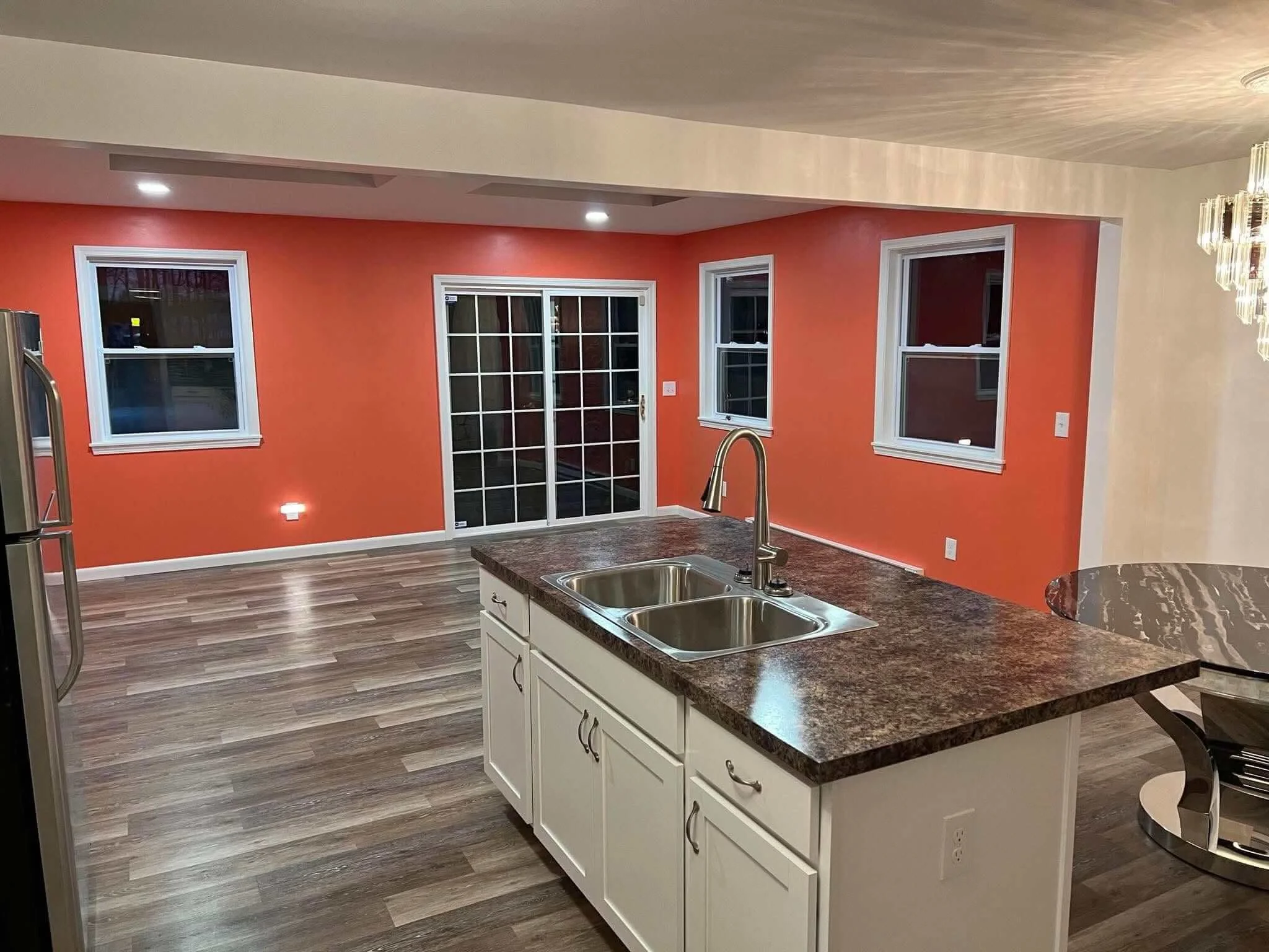 Open-concept kitchen addition in Kent, Ohio featuring a large granite-top island, custom white cabinets, vibrant orange walls, a sliding glass door, and recessed lighting by DLR.