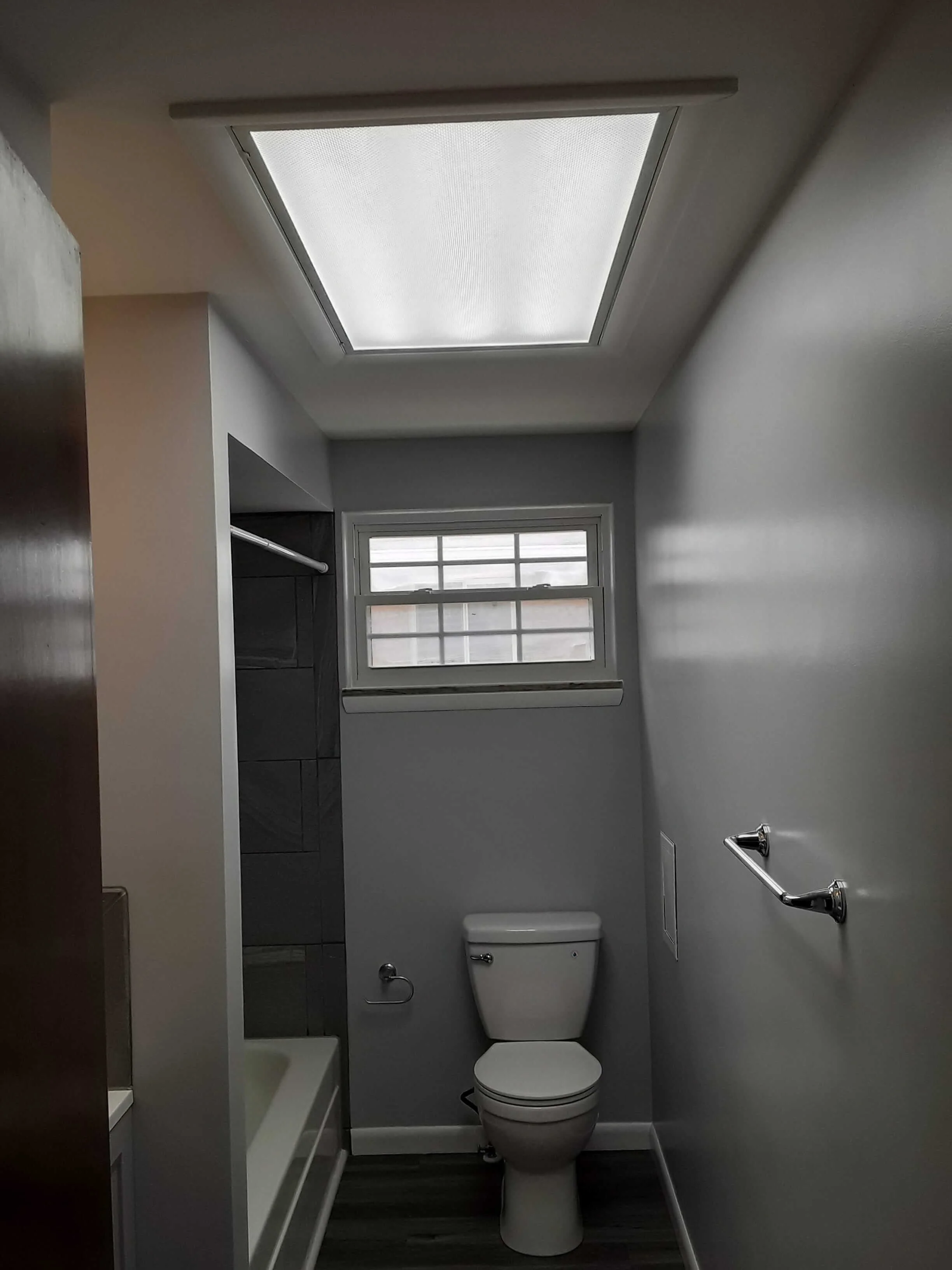 Modern bathroom remodel in Medina, Ohio showcasing large-format wall tiles, a newly replaced privacy glass window, updated toilet fixtures, and a new flooring layout by DLR.