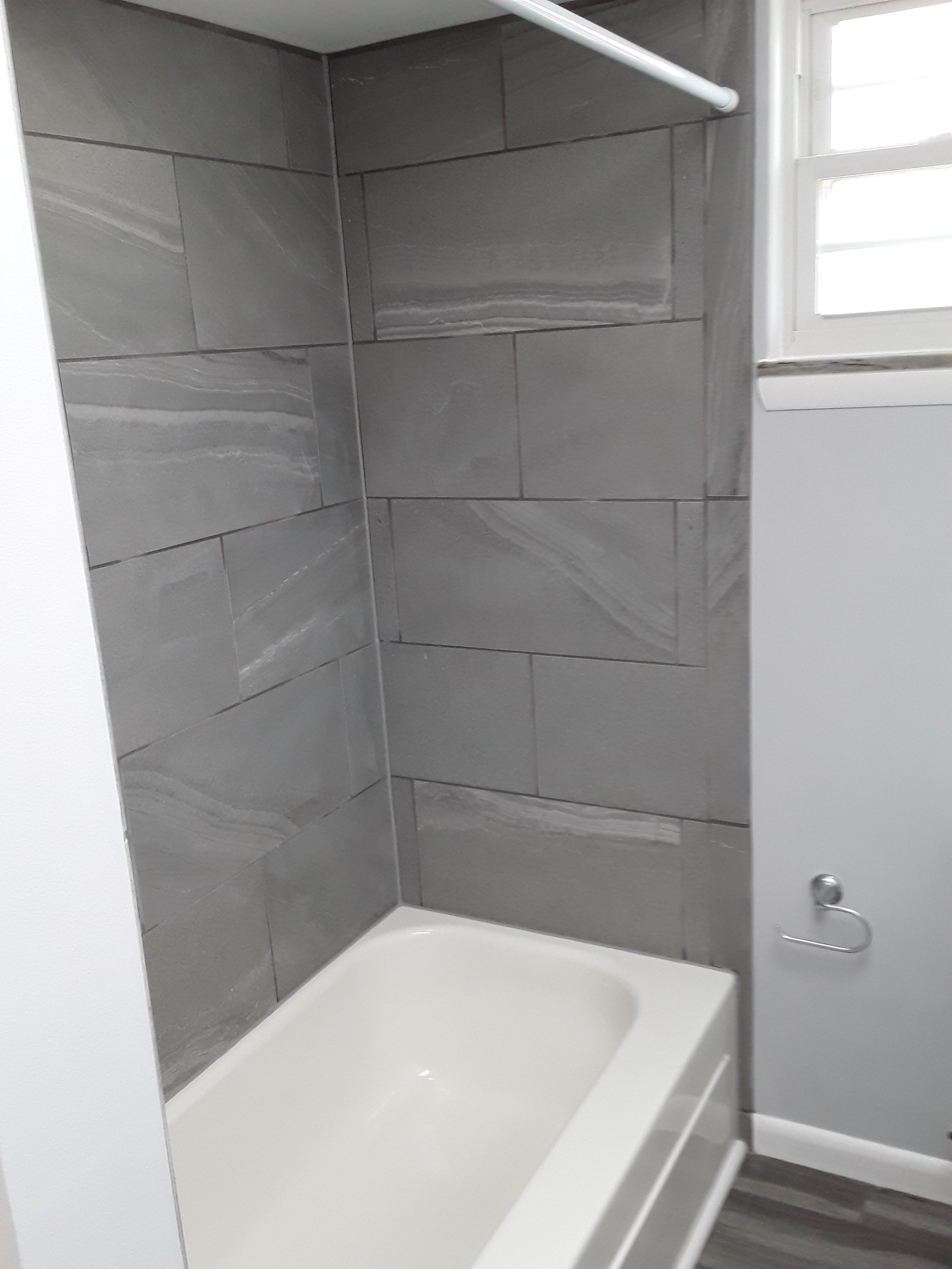 New bathtub with tiled shower surround, featuring clean grout lines and modern fixtures in renovated bathroom.