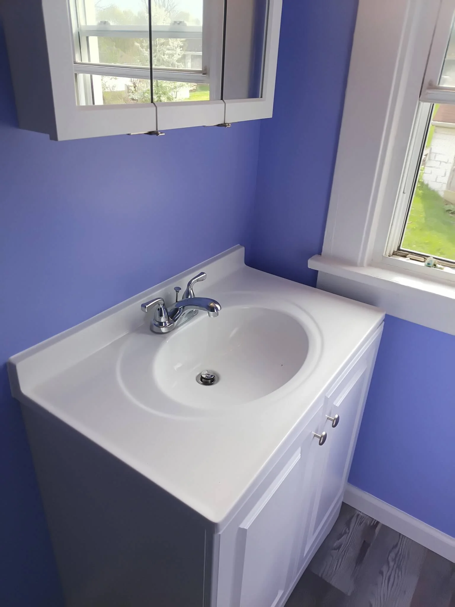 Completed down-to-the-studs bathroom renovation in Medina, Ohio featuring a clean white porcelain drop-in sink, modern chrome faucet, white vanity cabinet, and vibrant lavender walls by DLR Construction.