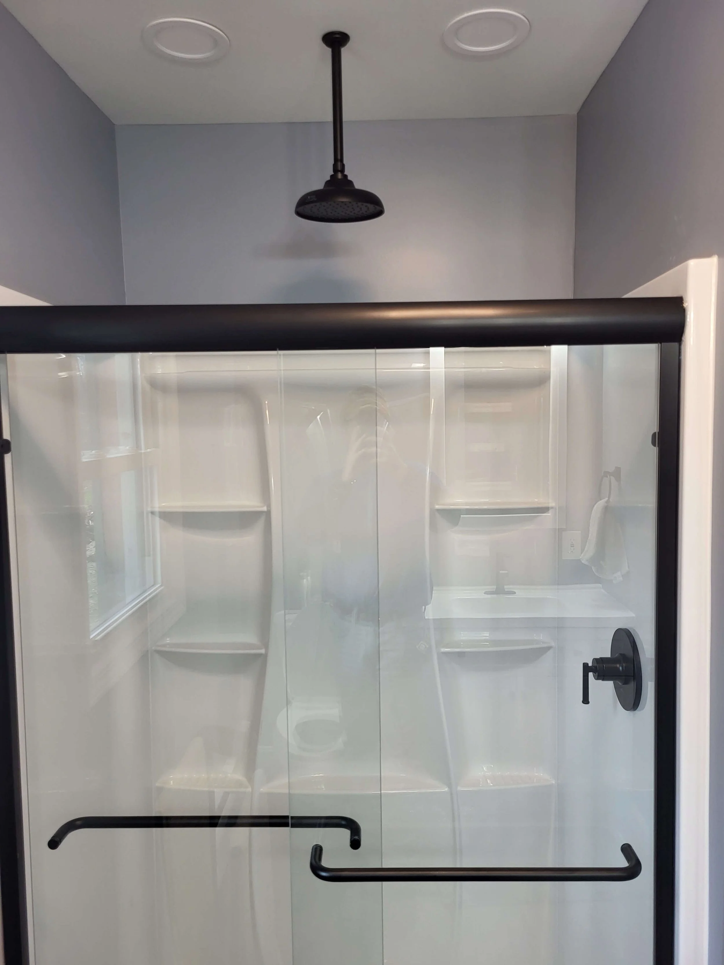 Modern custom shower with black sliding glass doors and rainfall shower head installation.