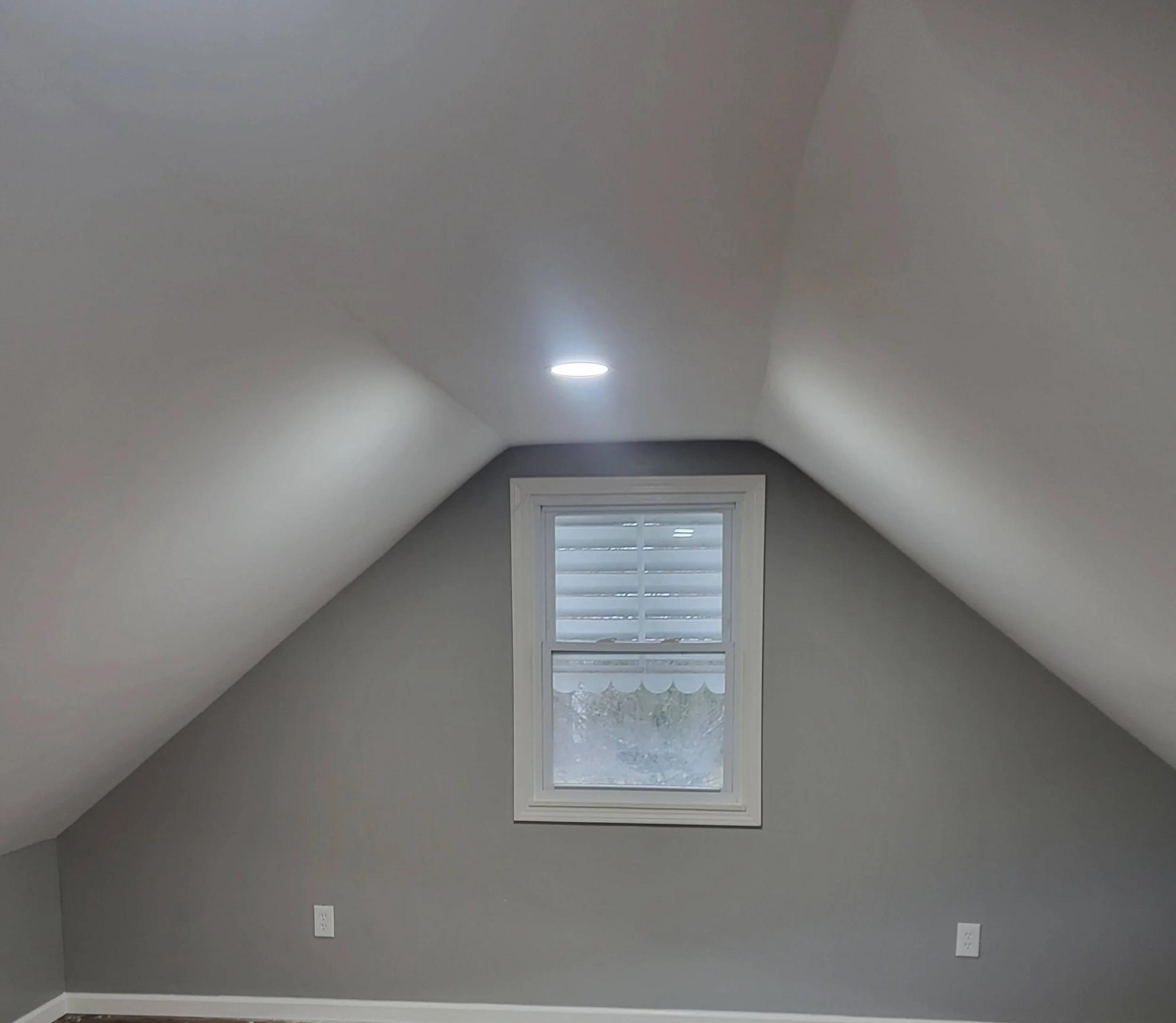 Finished attic renovation in Kent, Ohio showing smooth white refinished drywall walls, updated electrical outlets, and new energy-efficient recessed lighting under a vaulted ceiling by DLR Construction.