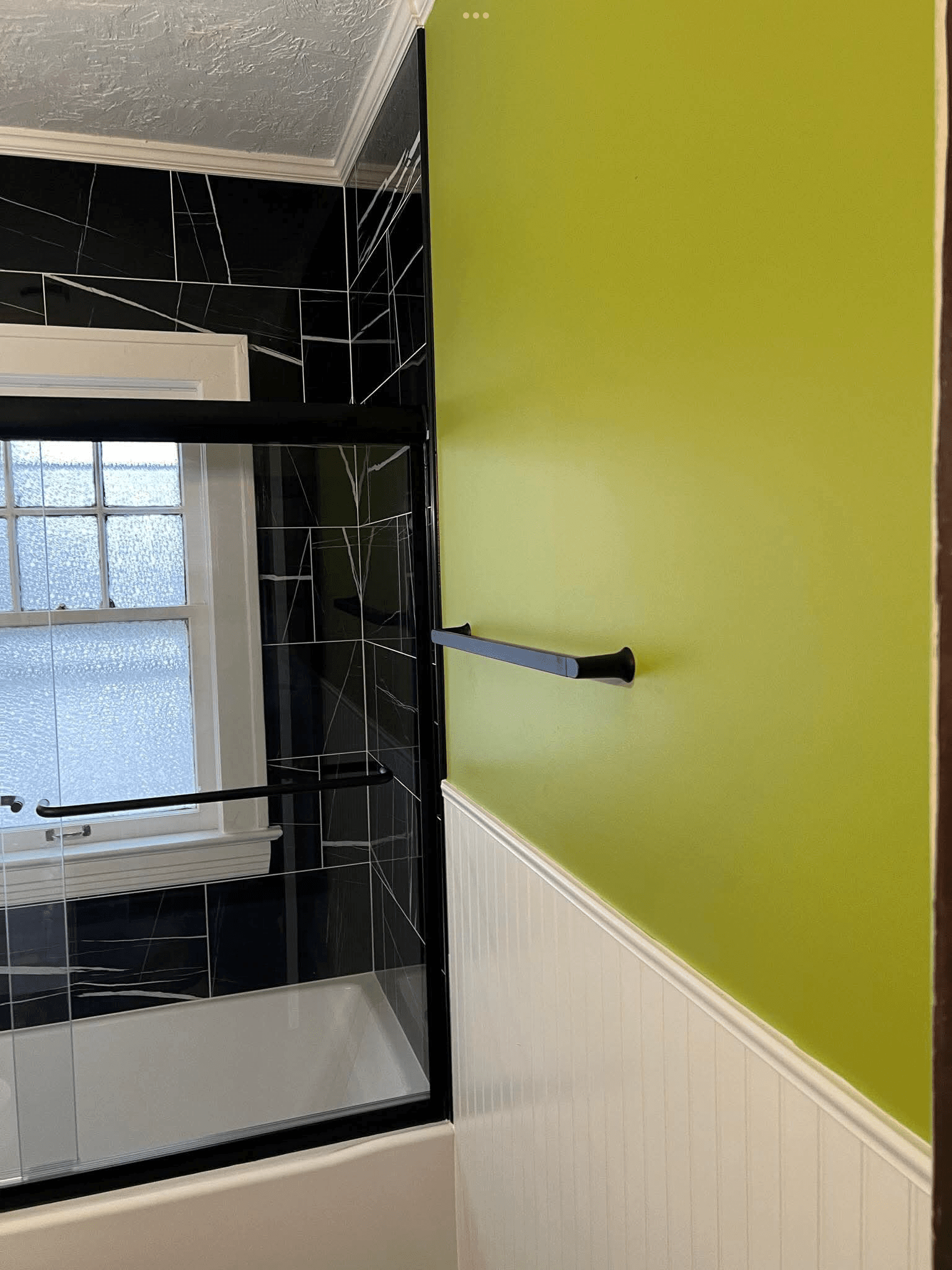 Close-up of green bathroom wall with white beadboard trim, towel bar, and black tile shower edge in remodeled bathroom.