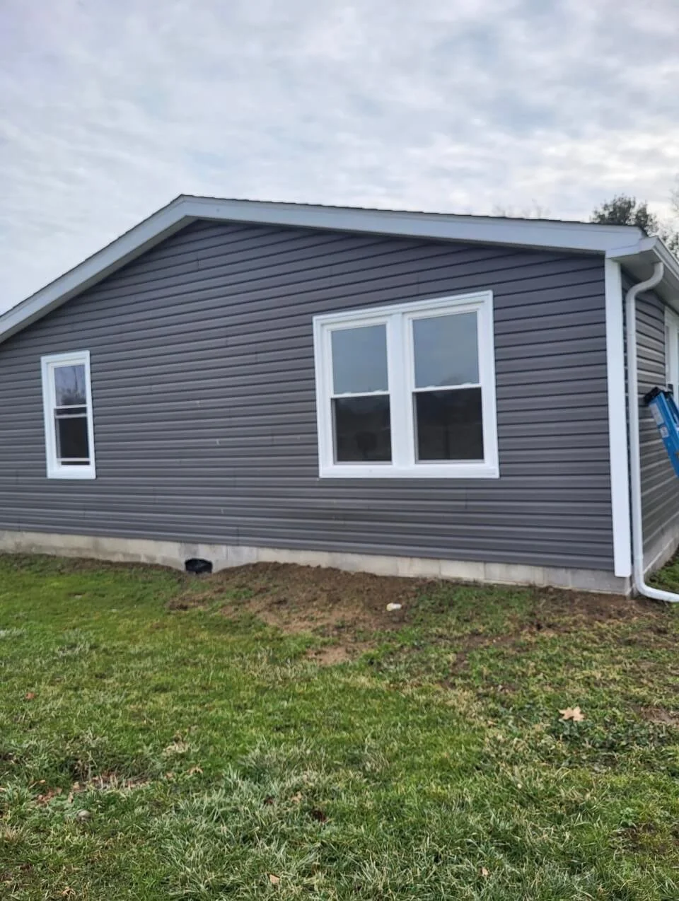 Heavy-gauge insulated gray vinyl siding installation with white-wrapped windows and custom aluminum trim fascia on a residential home renovation.