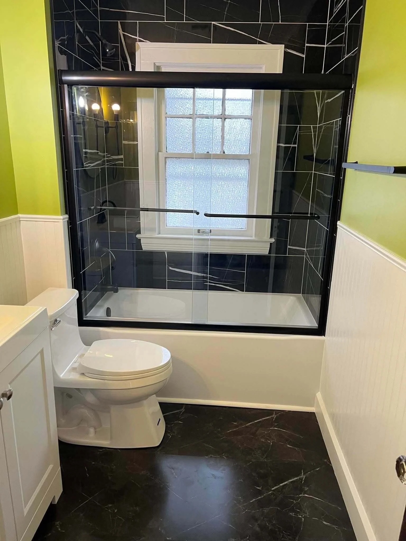 Modern bathtub shower combination with bold black tile walls and sliding glass shower doors in Northeast Ohio bathroom remodel.