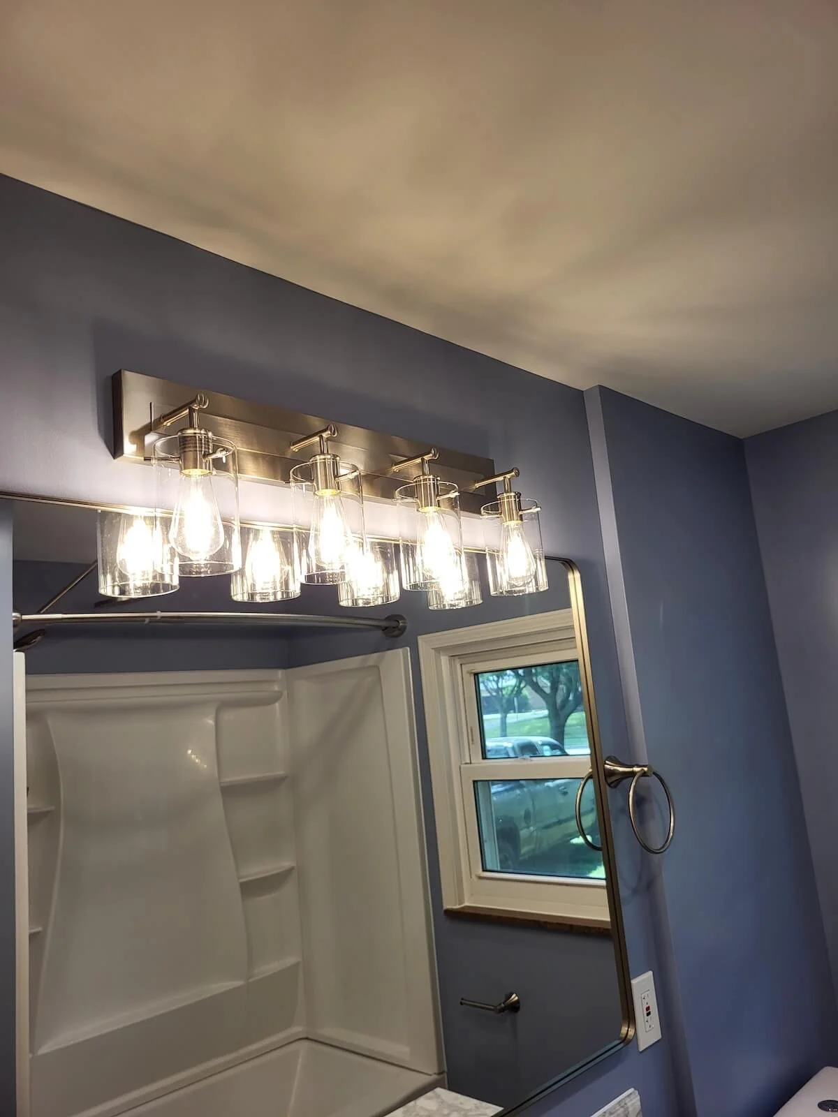 Modern chrome multi-bulb light bar installed above an antique flat mirror and dark bathroom vanity.